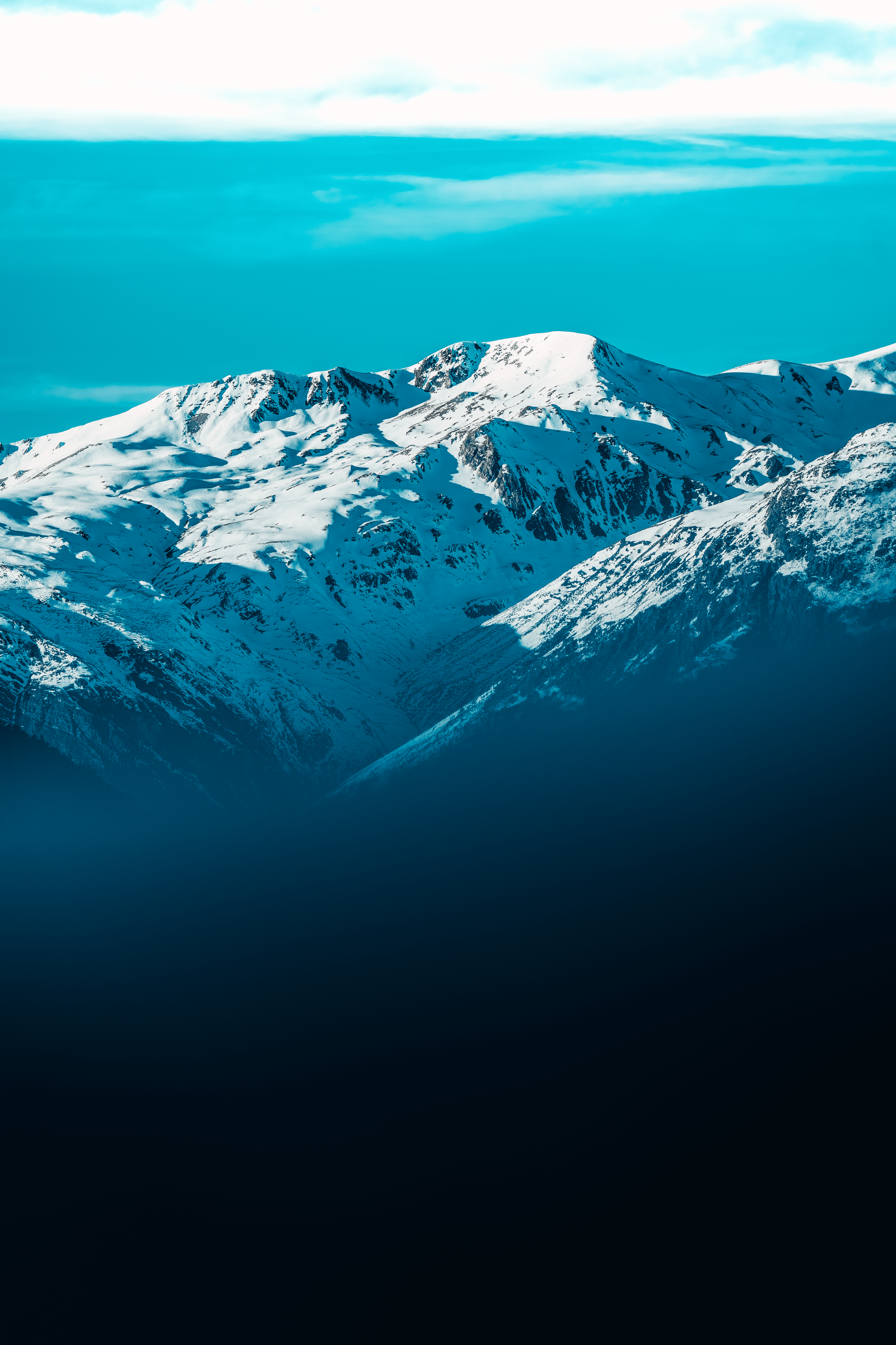 Montañas cubiertas de nieve y un cielo con nubes delgadas y azuladas.
