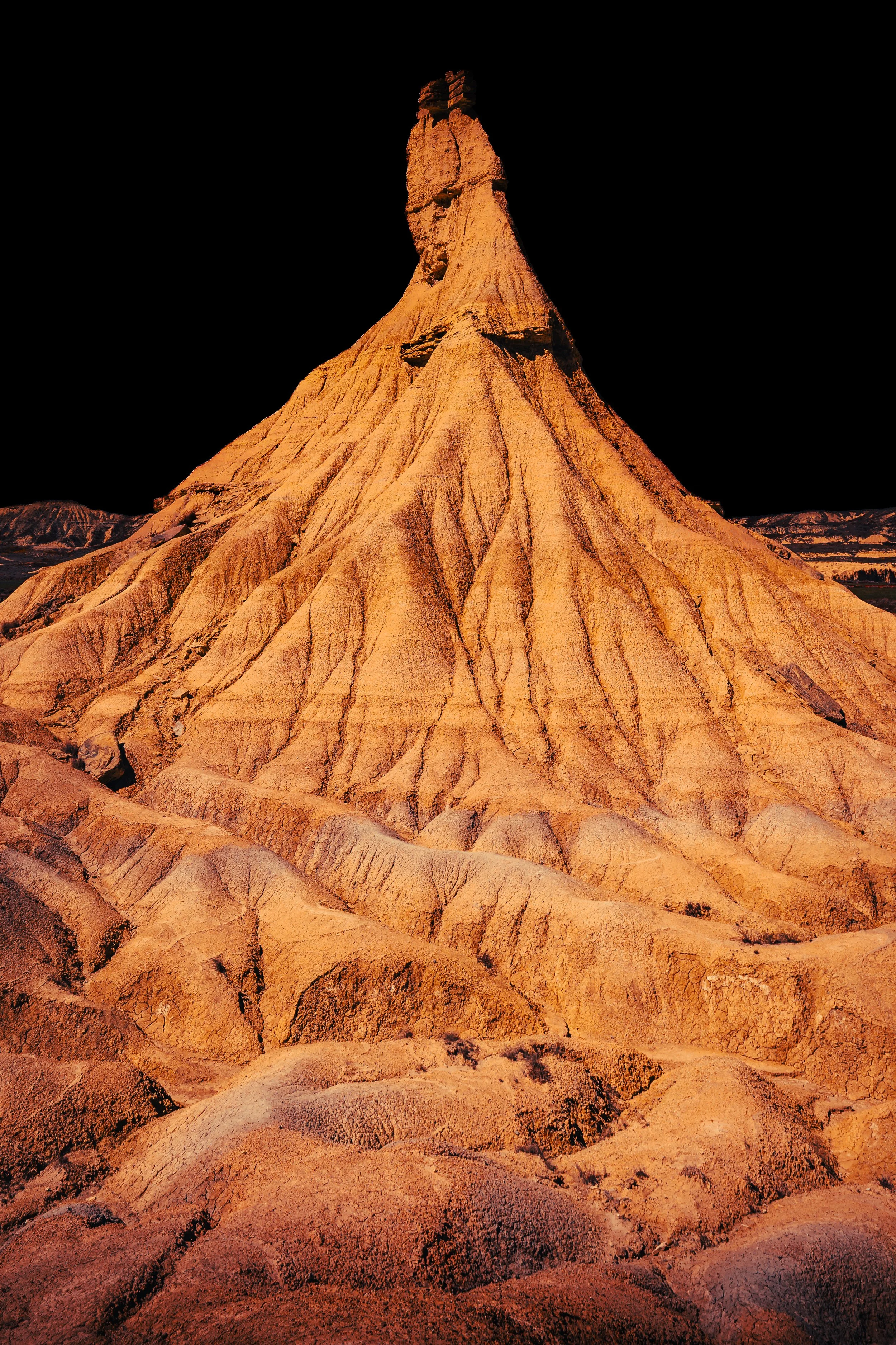Formación rocosa en tono anaranjado con picos en forma de pico, paisaje árido y montañoso en el fondo, noche oscura