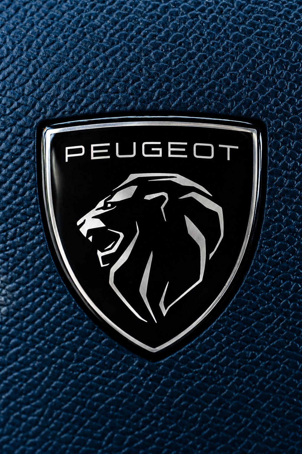 Emblema de Peugeot con un león en perfil en color negro y plata, sobre fondo texturizado azul oscuro.