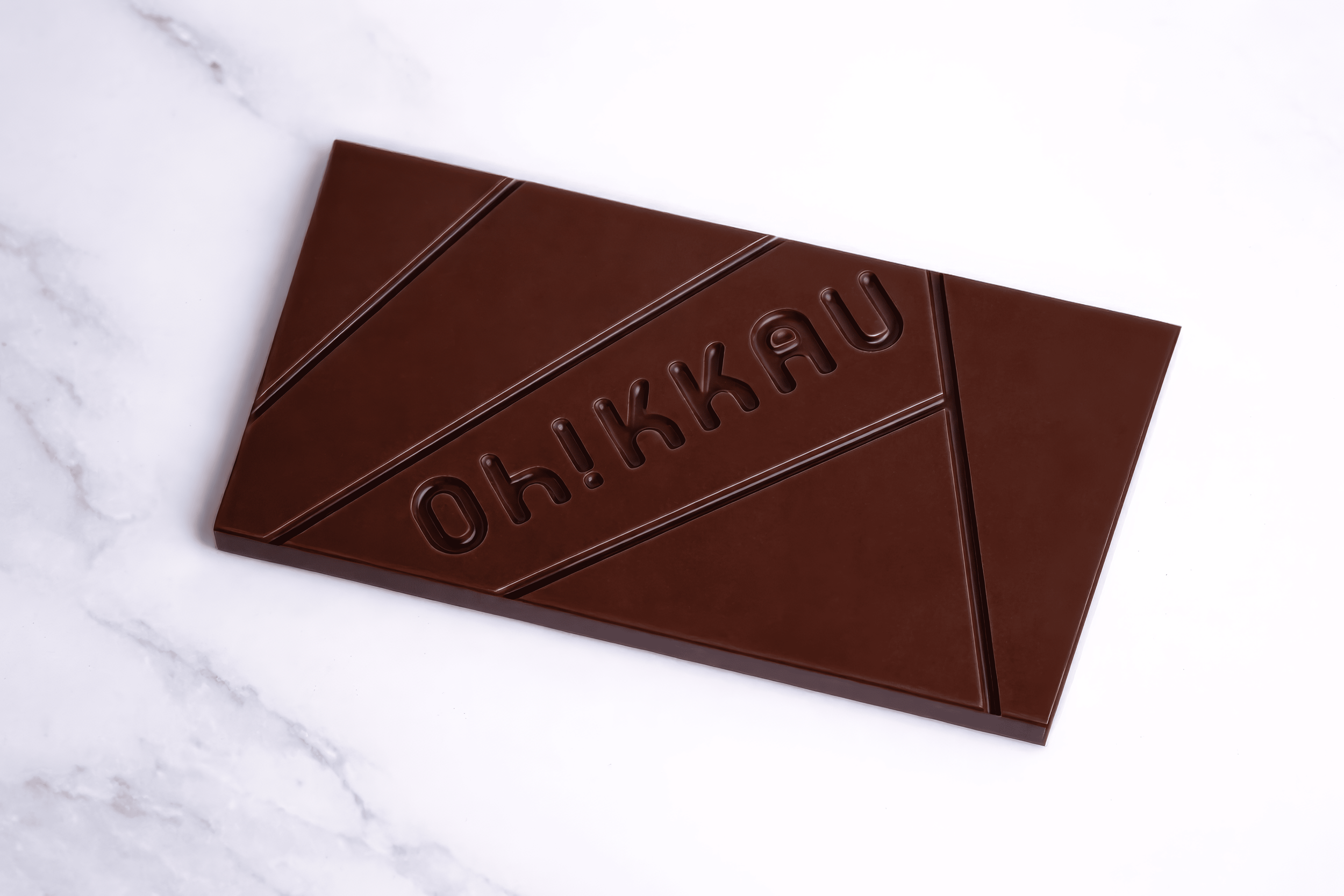 Una tableta de chocolate con la frase 'Oh! KAKAU' grabada en ella, sobre una superficie de mármol blanco.