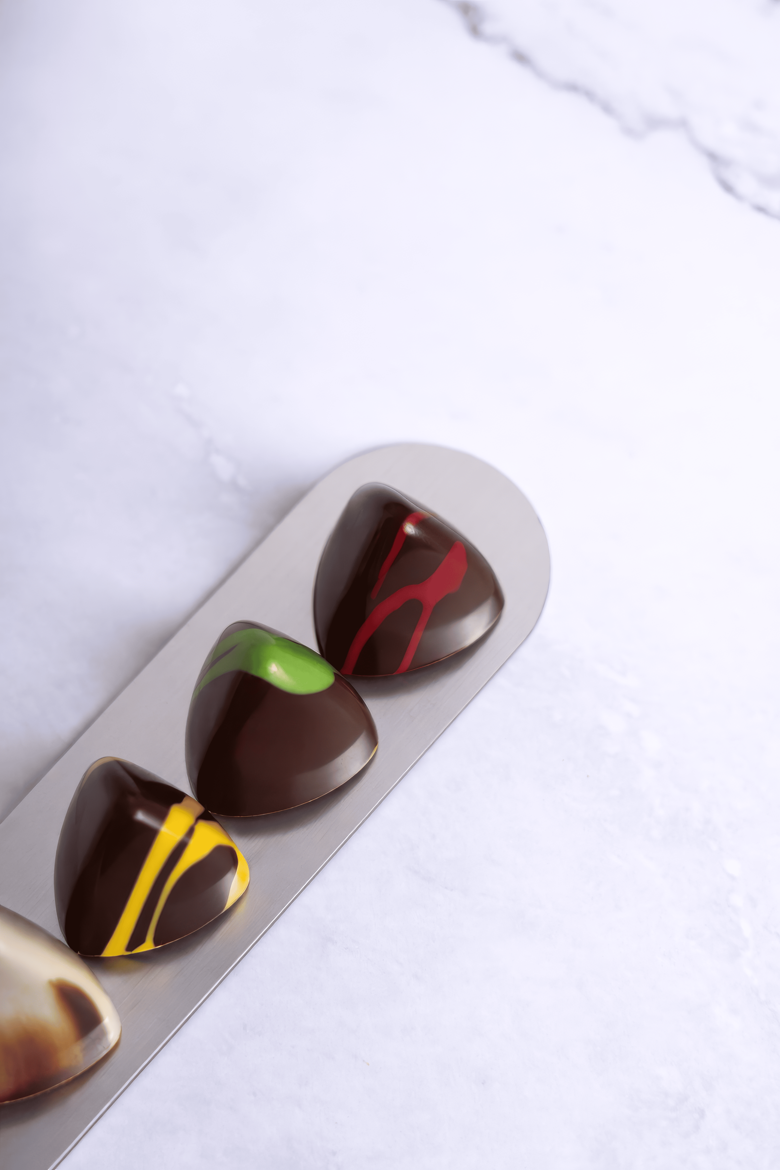 Tabla con cuatro bombones de chocolate decorados con diferentes colores y patrones.