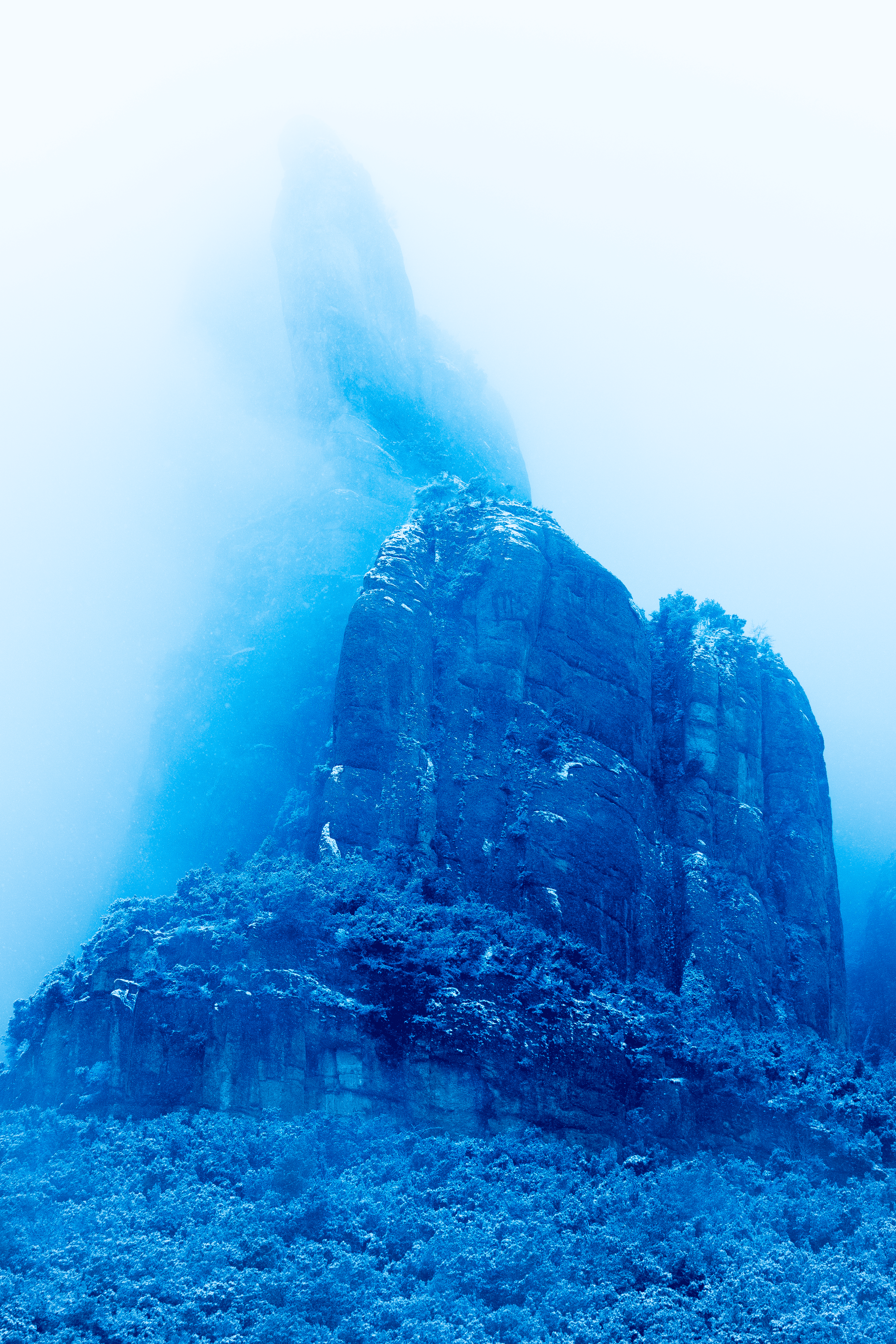 una montaña cubierta de nieve y niebla, con formaciones rocosas altas y vegetación en la base