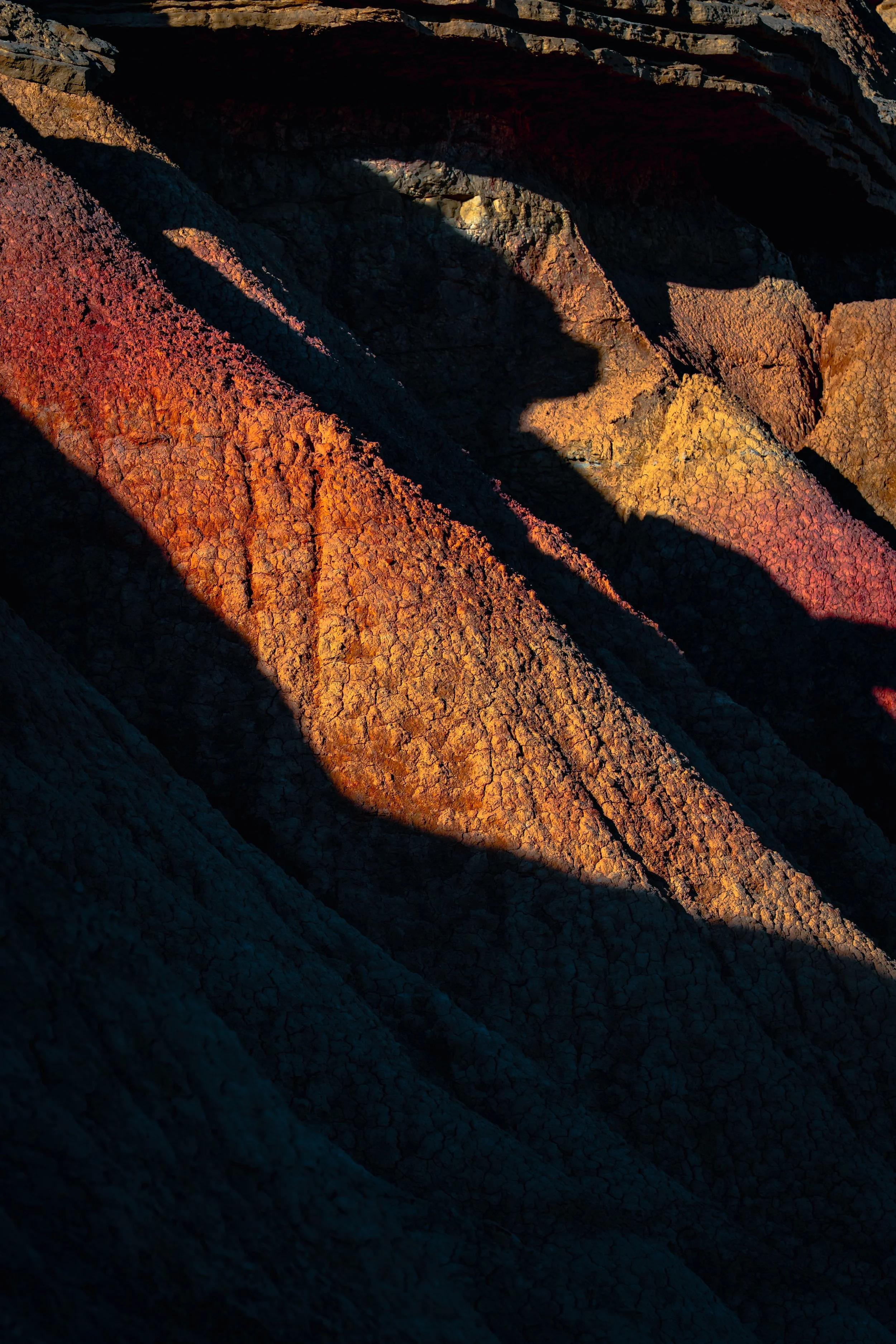 Superficie de tierra árida con colores rojos, anaranjados y oscuros, con sombras pronunciadas y textura rugged.