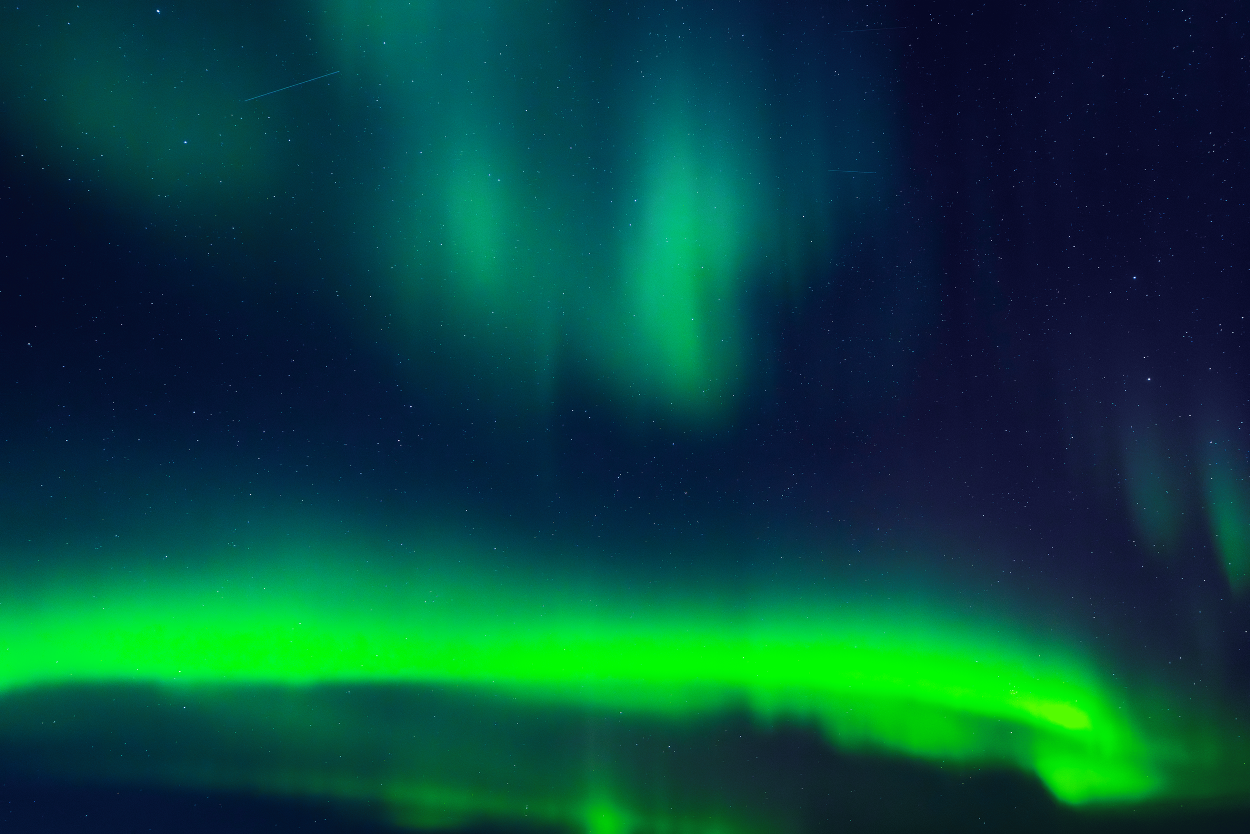 Aurora boreal en el cielo nocturno con estrellas sobre un paisaje oscuro.