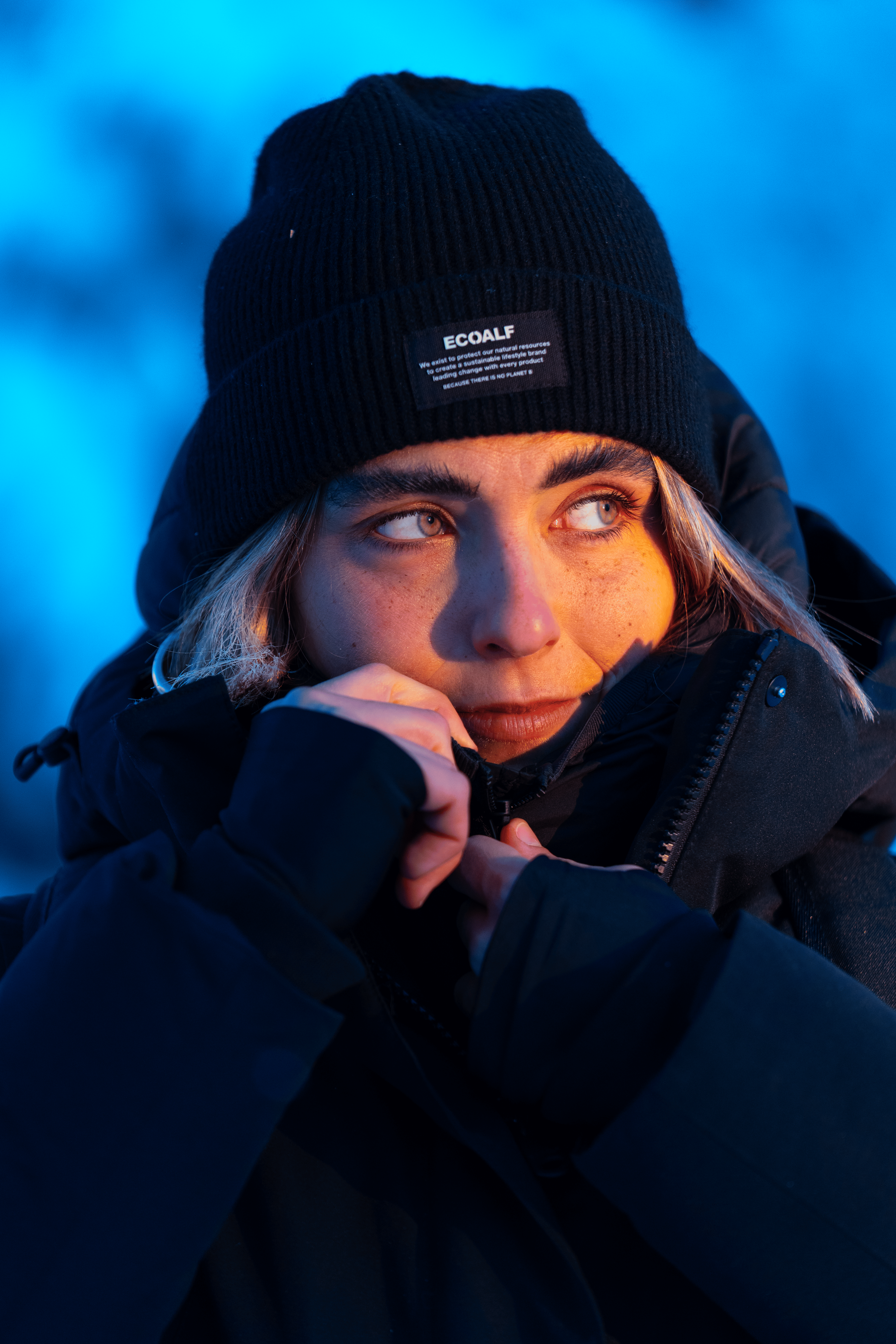 Joven con gorro negro y chaqueta abrigadora en un entorno frío, mirando hacia un lado con expresión pensativa.