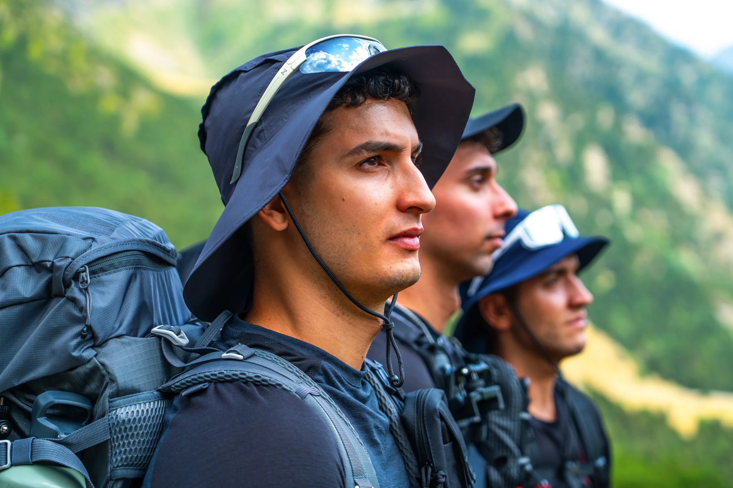 Grupo de jóvenes hombres de perfil con mochilas en una caminata en un entorno natural.
