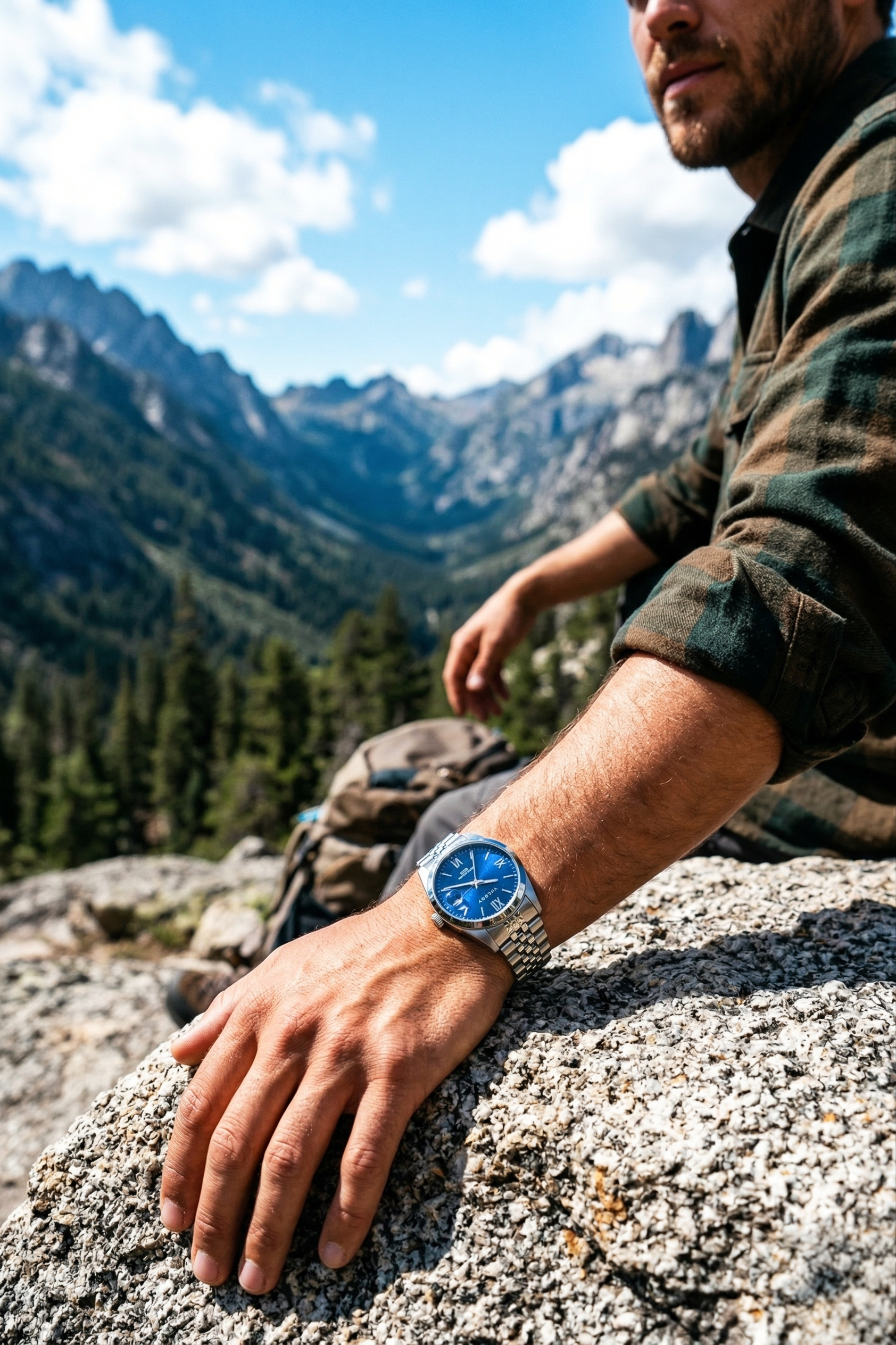 Hombre con reloj de pulsera apoyado sobre una roca en un paisaje de montañas y cielo con nubes.
