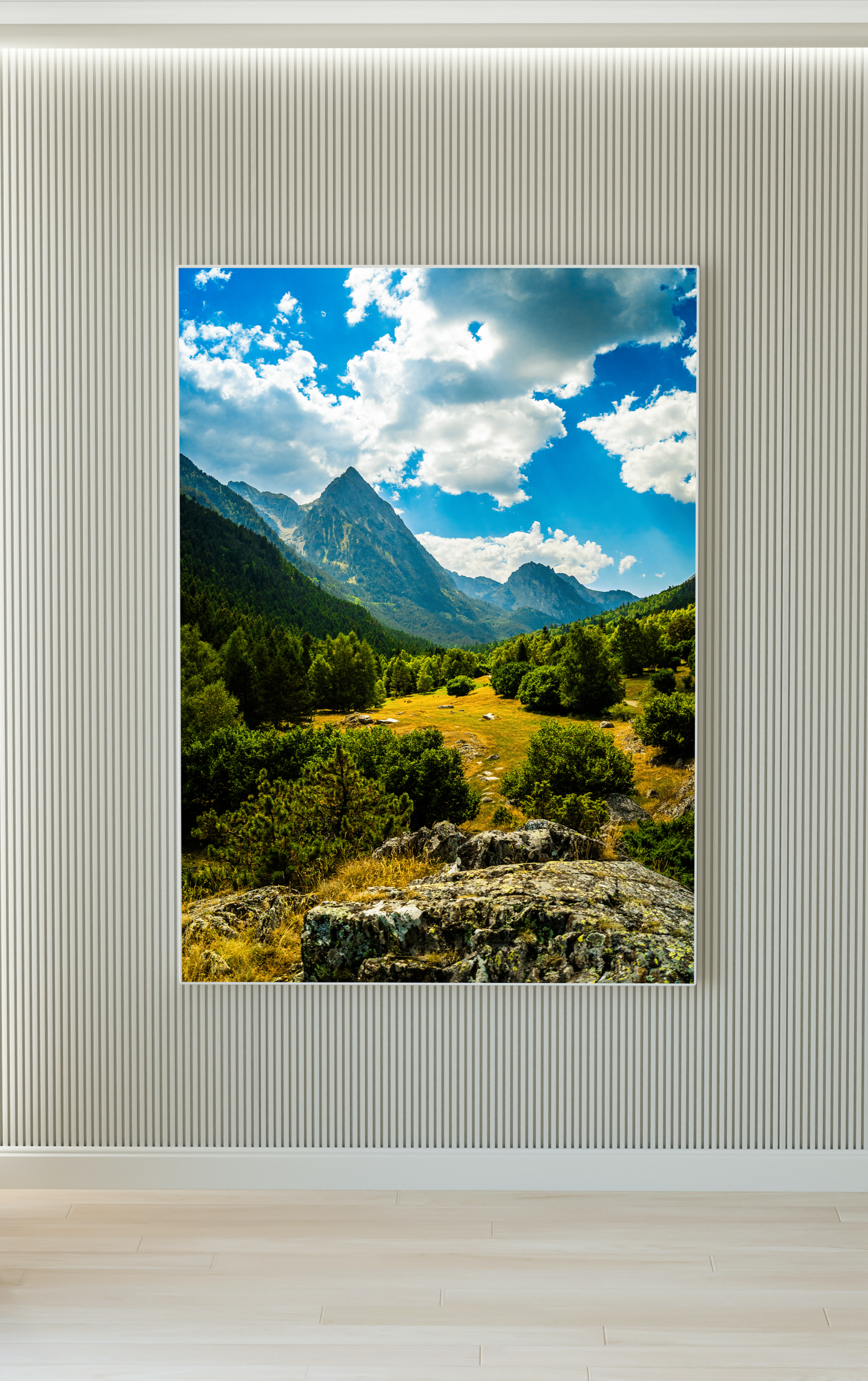 Vista de montañas con picos escarpados, un valle verde con árboles y rocas, cielo con nubes blancas y cielo azul.