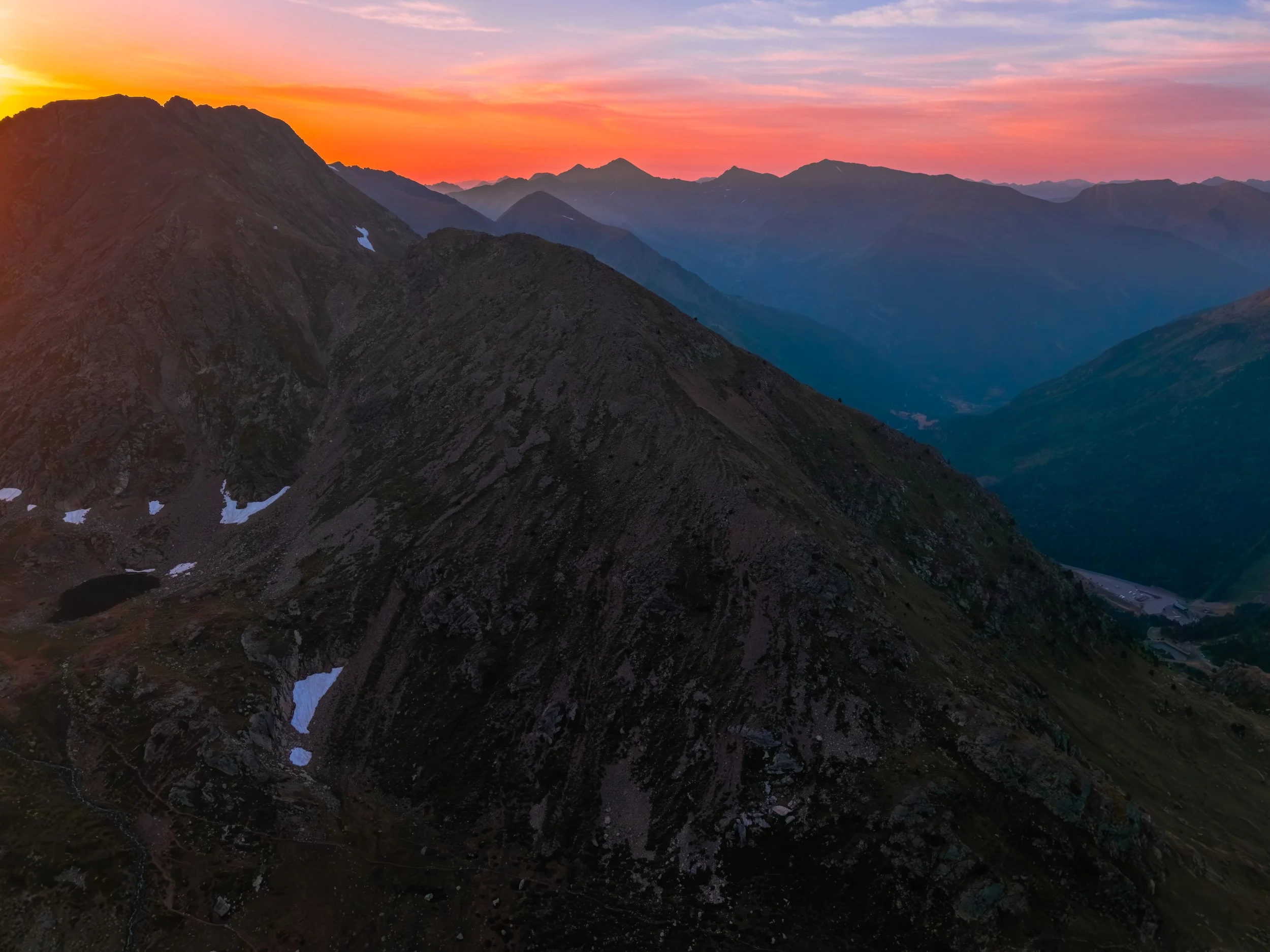 Paisaje de montañas al atardecer con picos rocosos y cielo con tonos naranjas, rosados y azules.