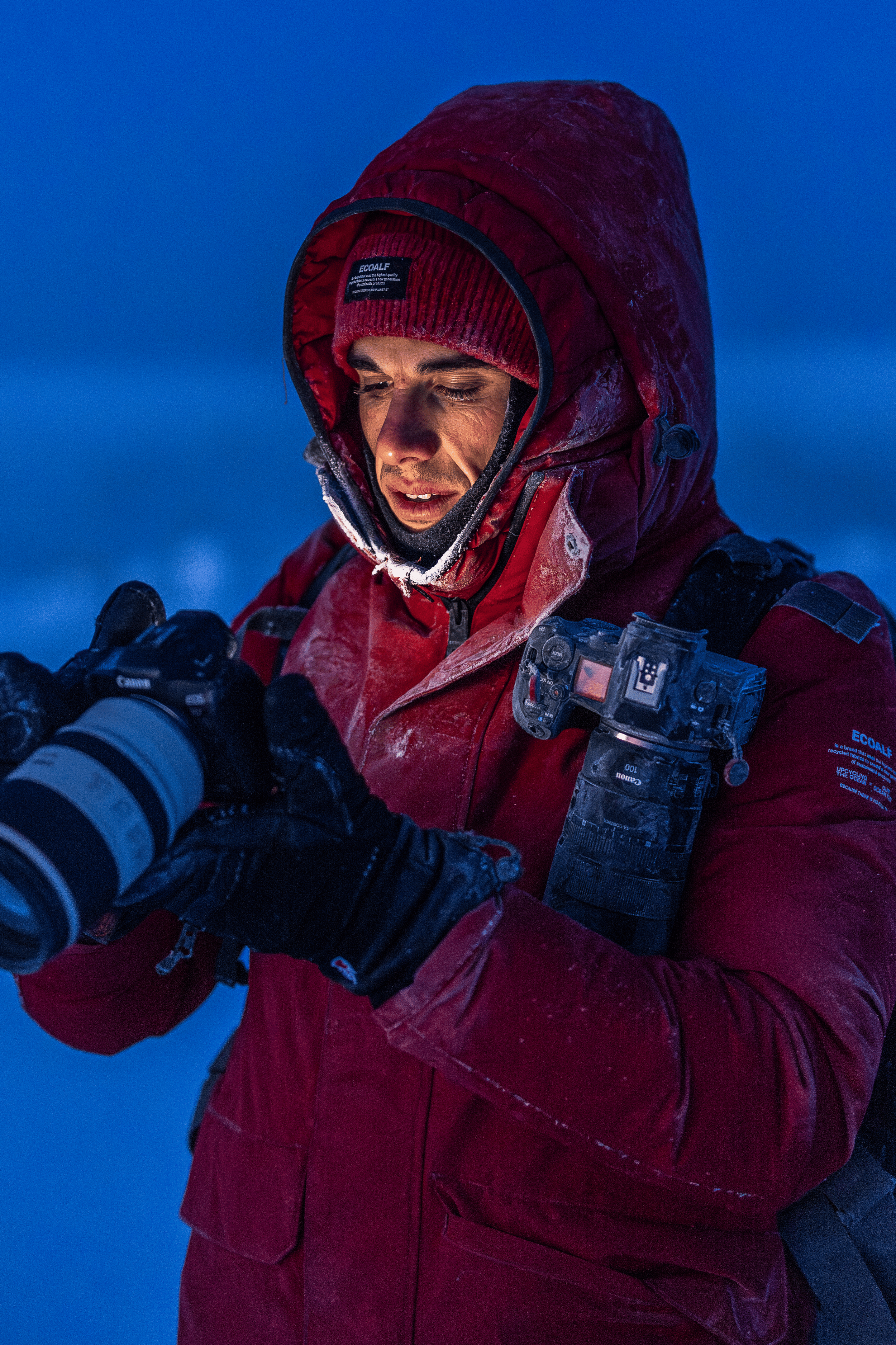 Una persona con ropa de abrigo en un entorno helado, revisando una cámara fotográfica.