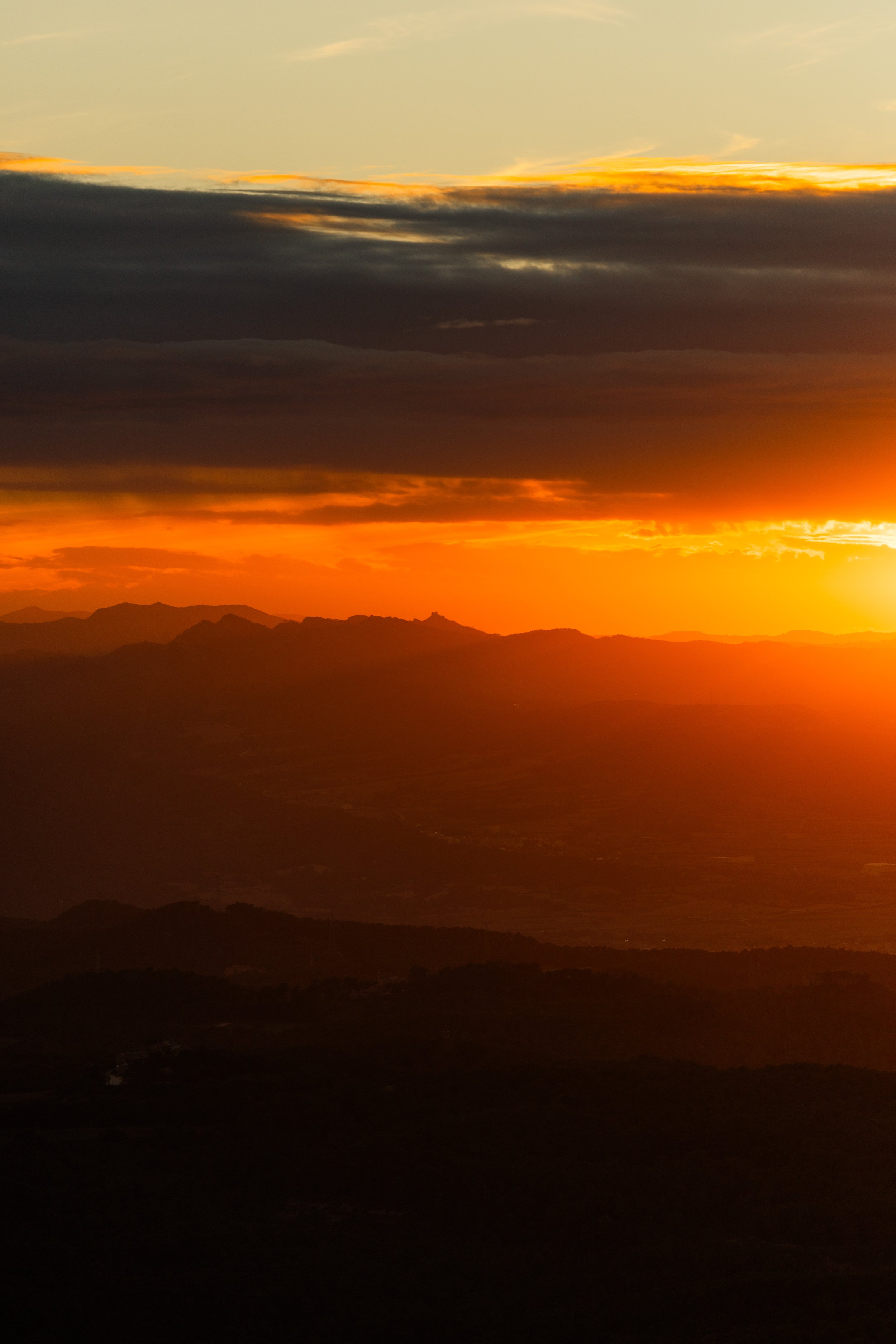 Atardecer con nubes oscuras sobre montañas y un horizonte naranja brillante.