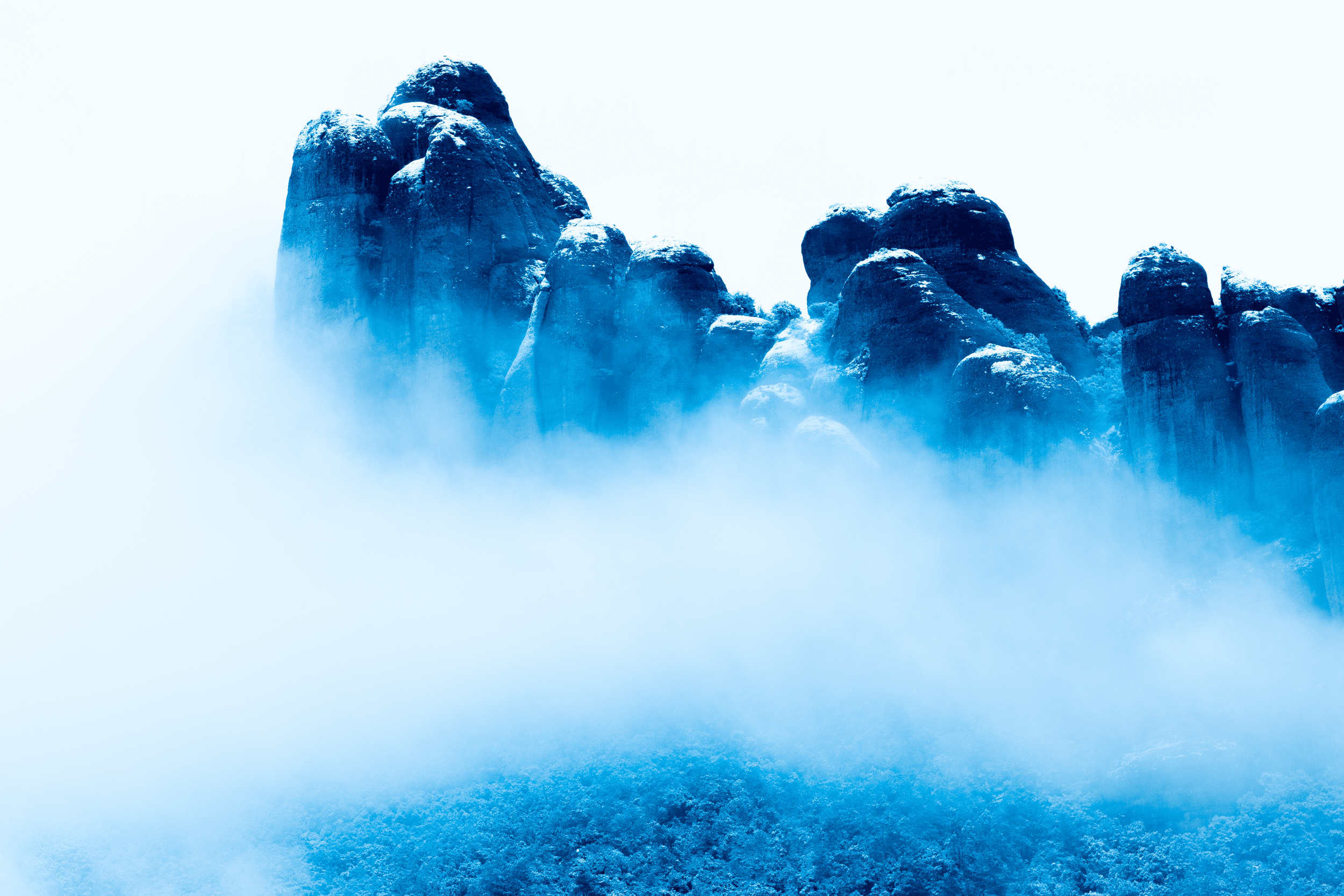 Montañas cubiertas de nieve en medio de una neblina o nubes en tonos azules.
