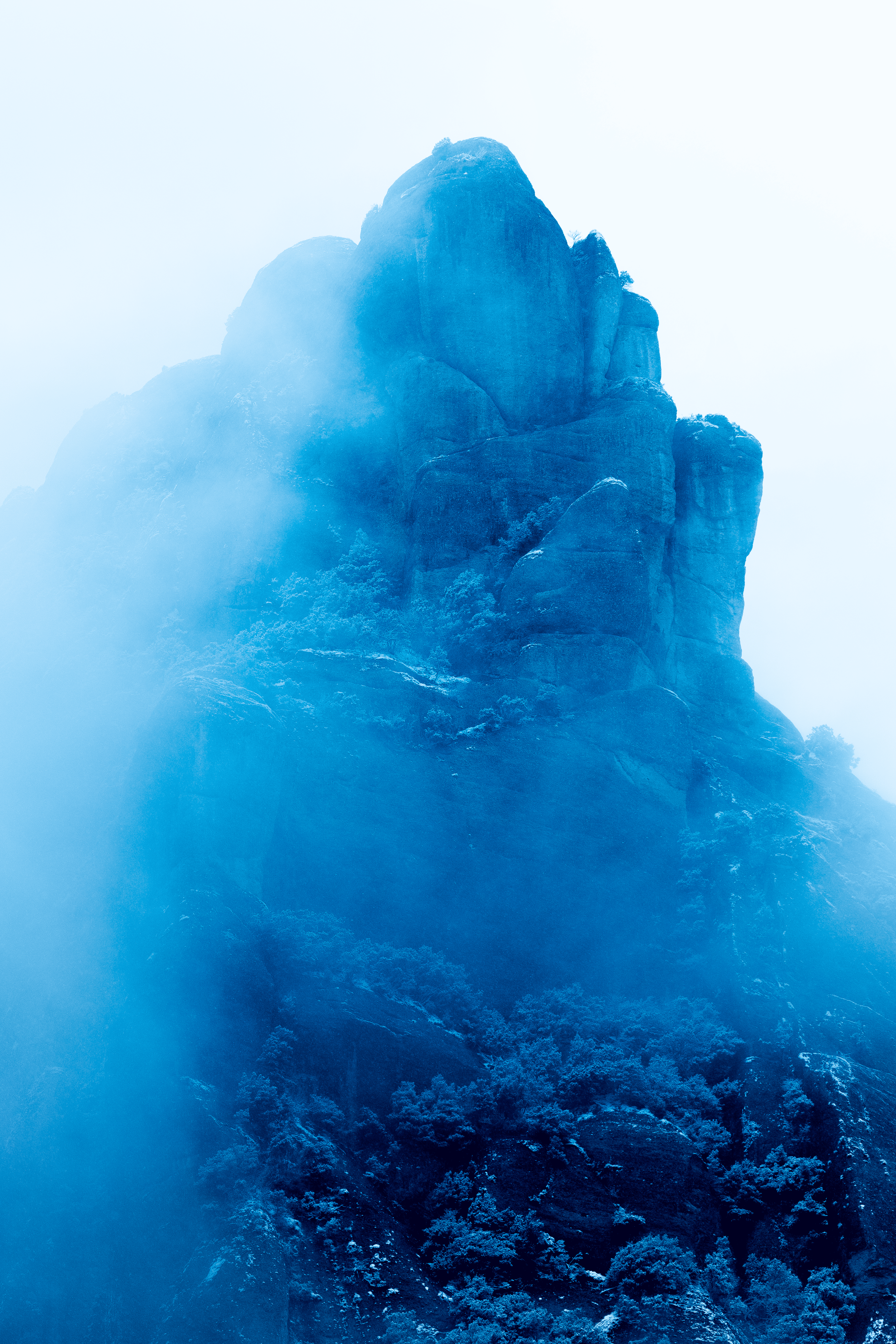 Una montaña rocosa con vegetación en la base, envuelta en una neblina azul.