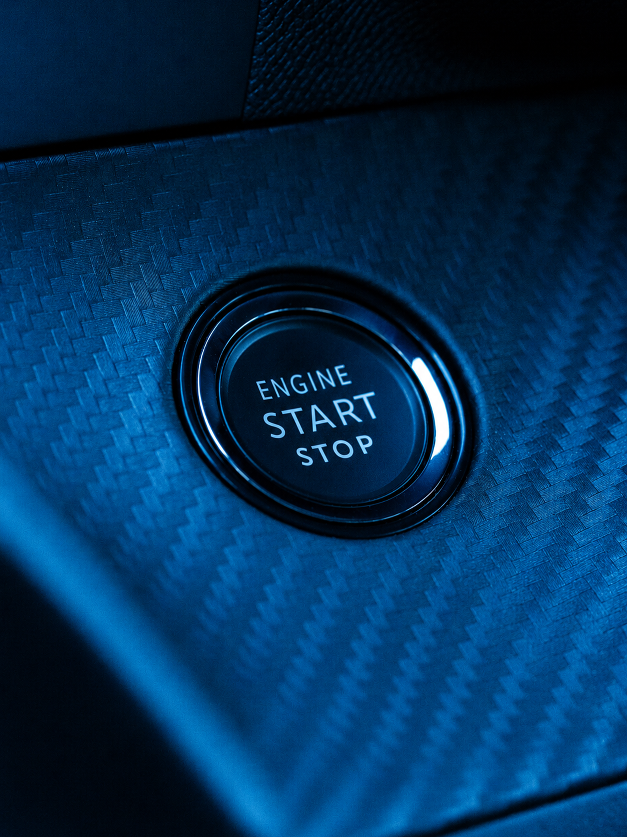 Botón de encendido/apagado del motor de un coche en un panel con textura metálica y luz azul.