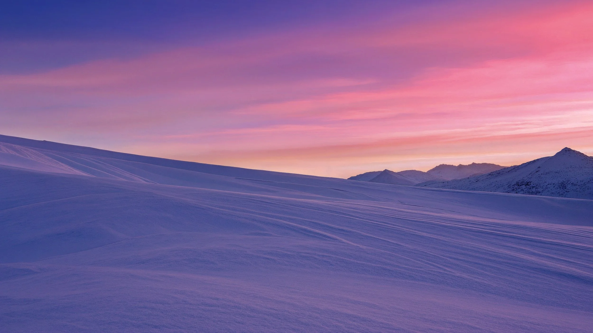 Paisaje con dunas de nieve bajo un cielo rosa y púrpura al atardecer o amanecer, con montañas de fondo.