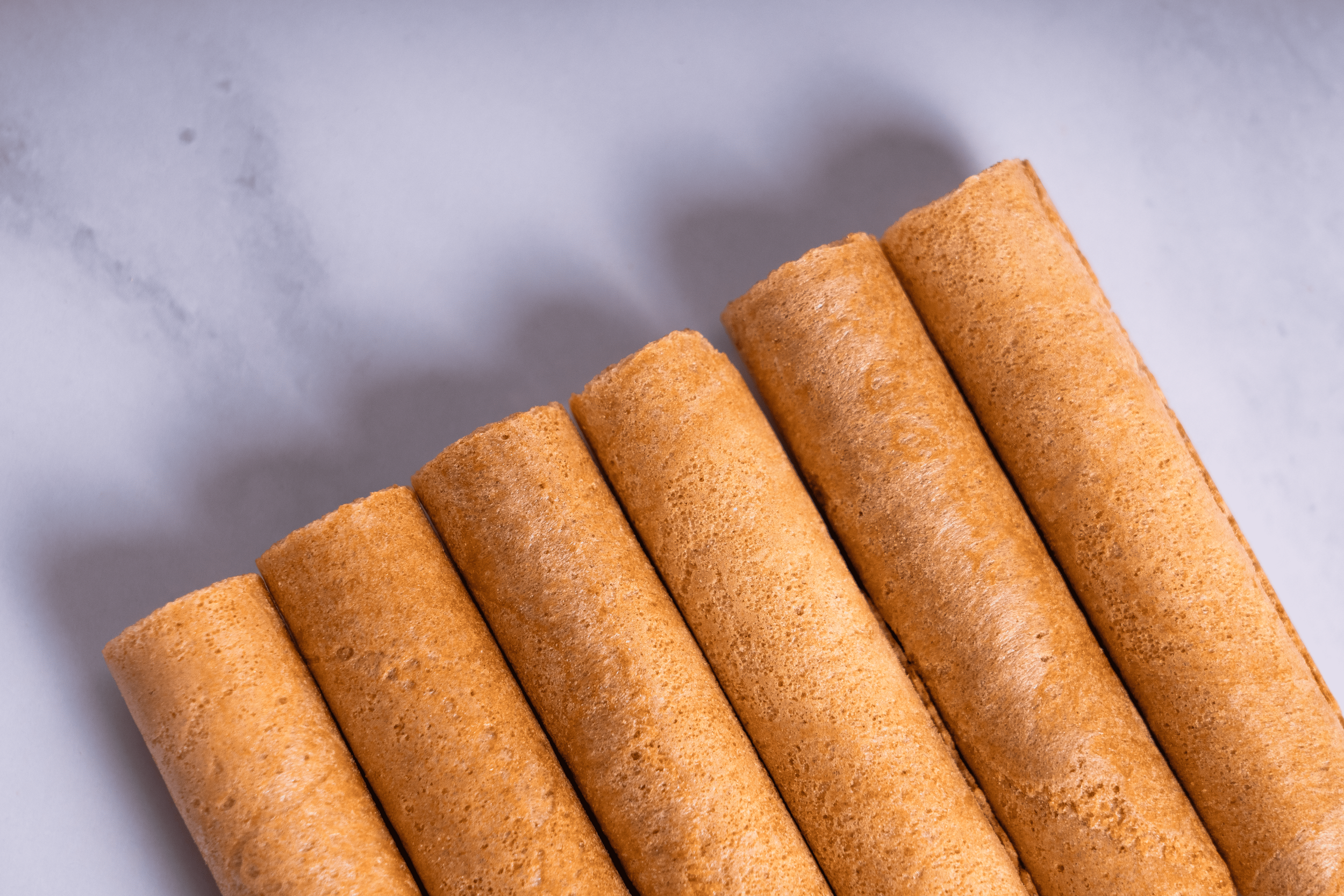 Cinco rollos de galletas de color dorado en línea sobre una superficie blanca.