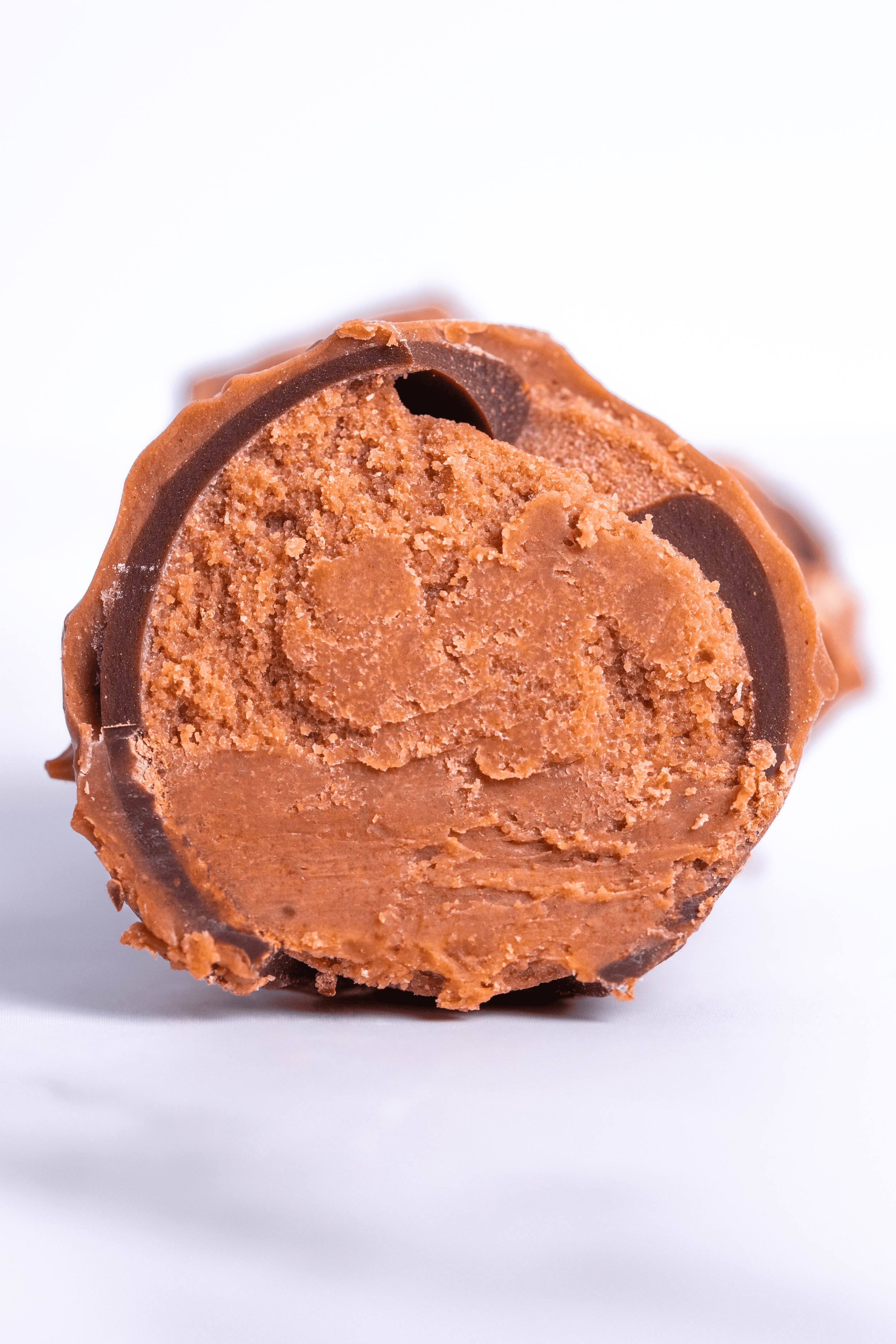 Vista en primer plano de un bombón de chocolate con relleno de dulce de leche, con apariencia cremosa y textura suave, sobre fondo blanco.