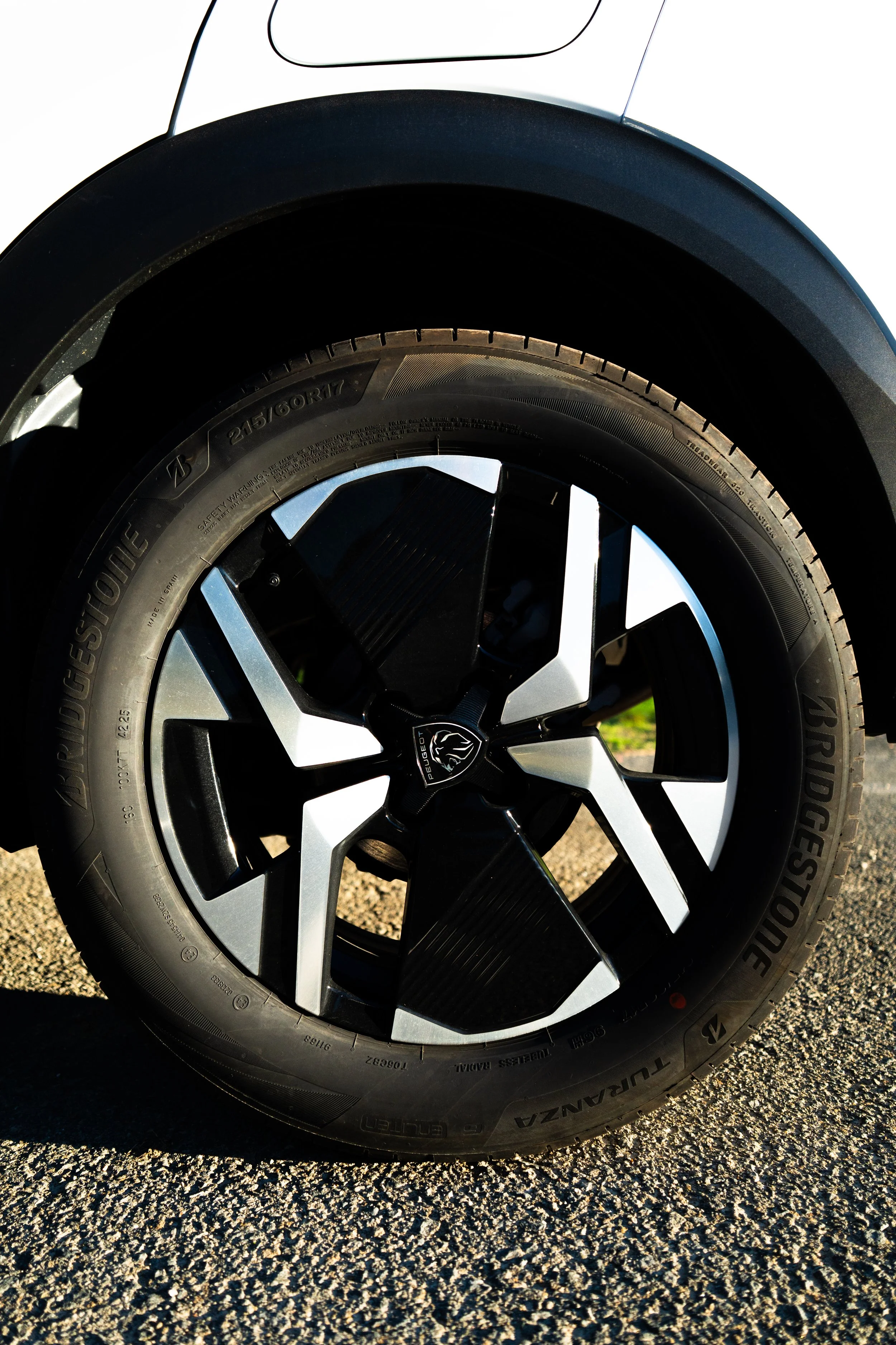 Primer plano de una llanta de neumático de automóvil con rueda de diseño moderno en un pavimento rugoso, con marca Bridgestone y tamaño 215/60 R17