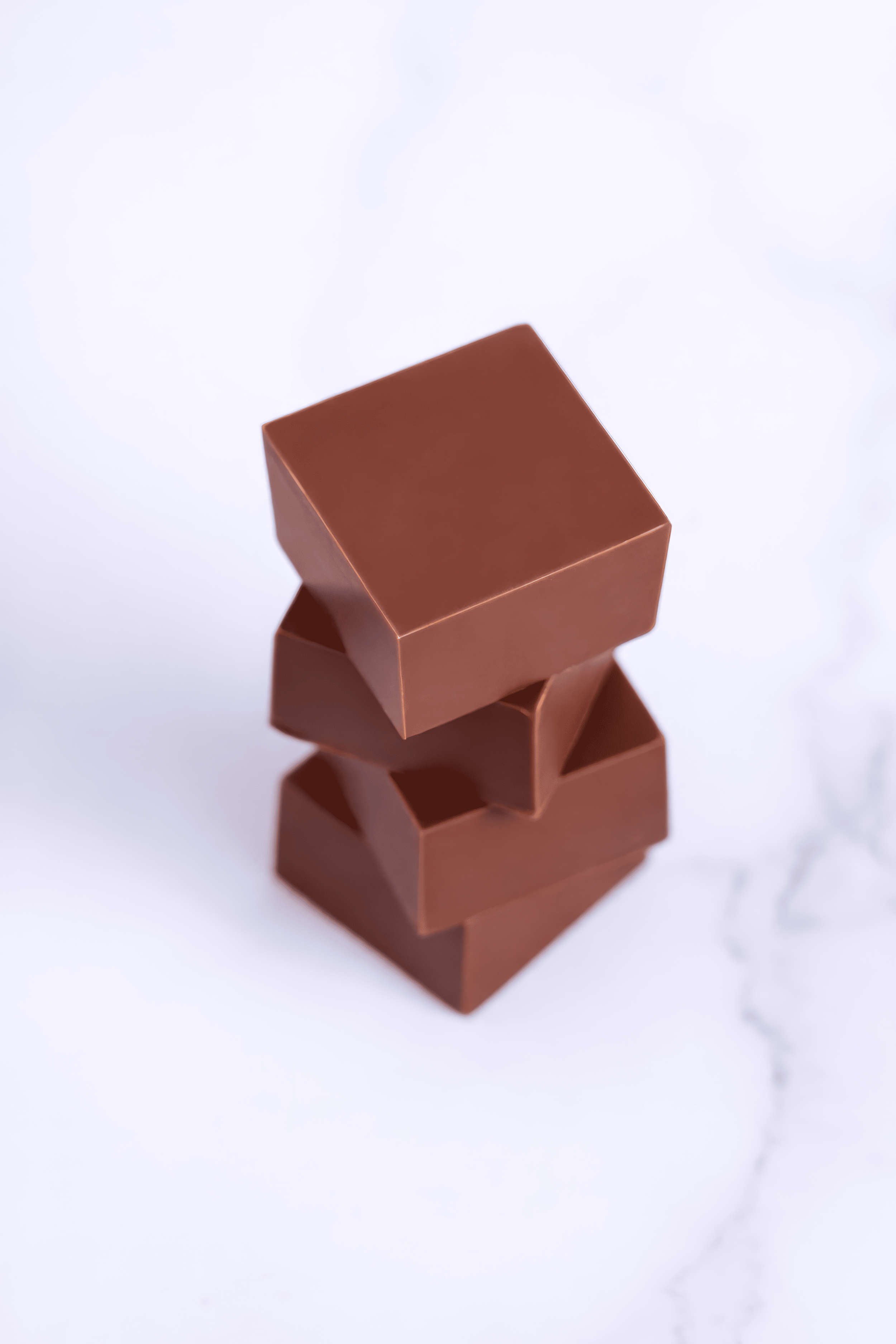 Tres cajas de chocolate apiladas en línea sobre una superficie blanca