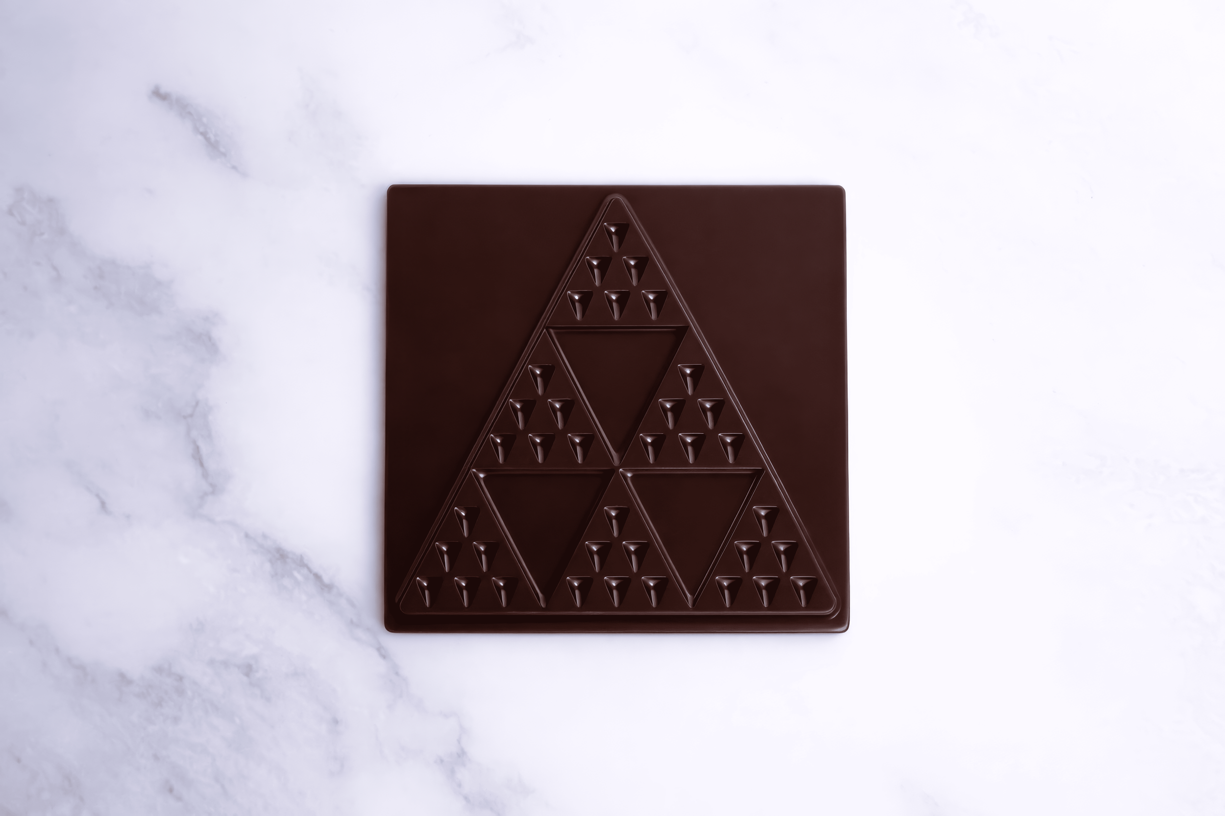Tabla de chocolate con diseño de triángulos y pequeños picos en una superficie blanca.
