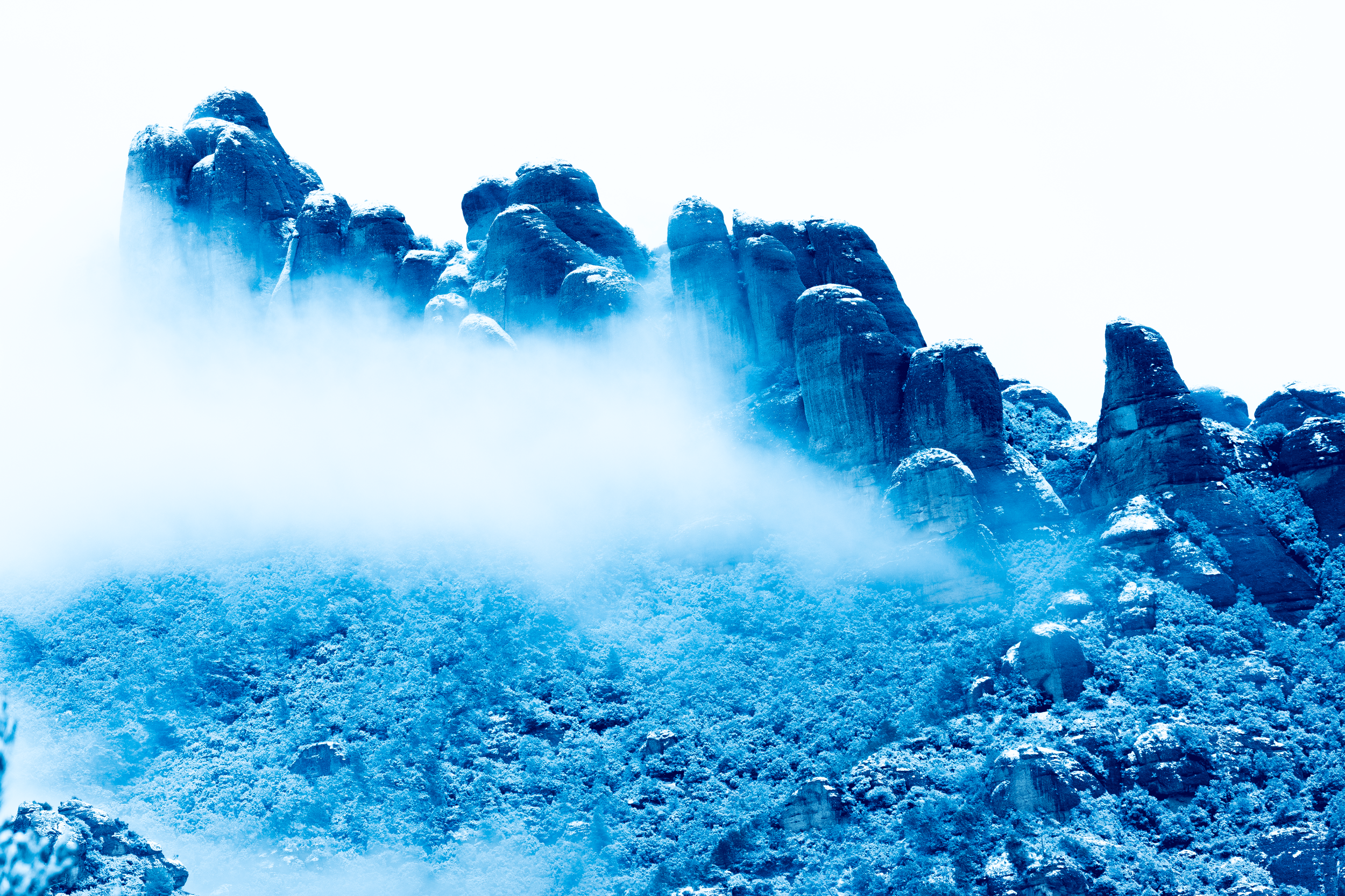 Montañas rocosas cubiertas de nieve con niebla y nubes bajas.