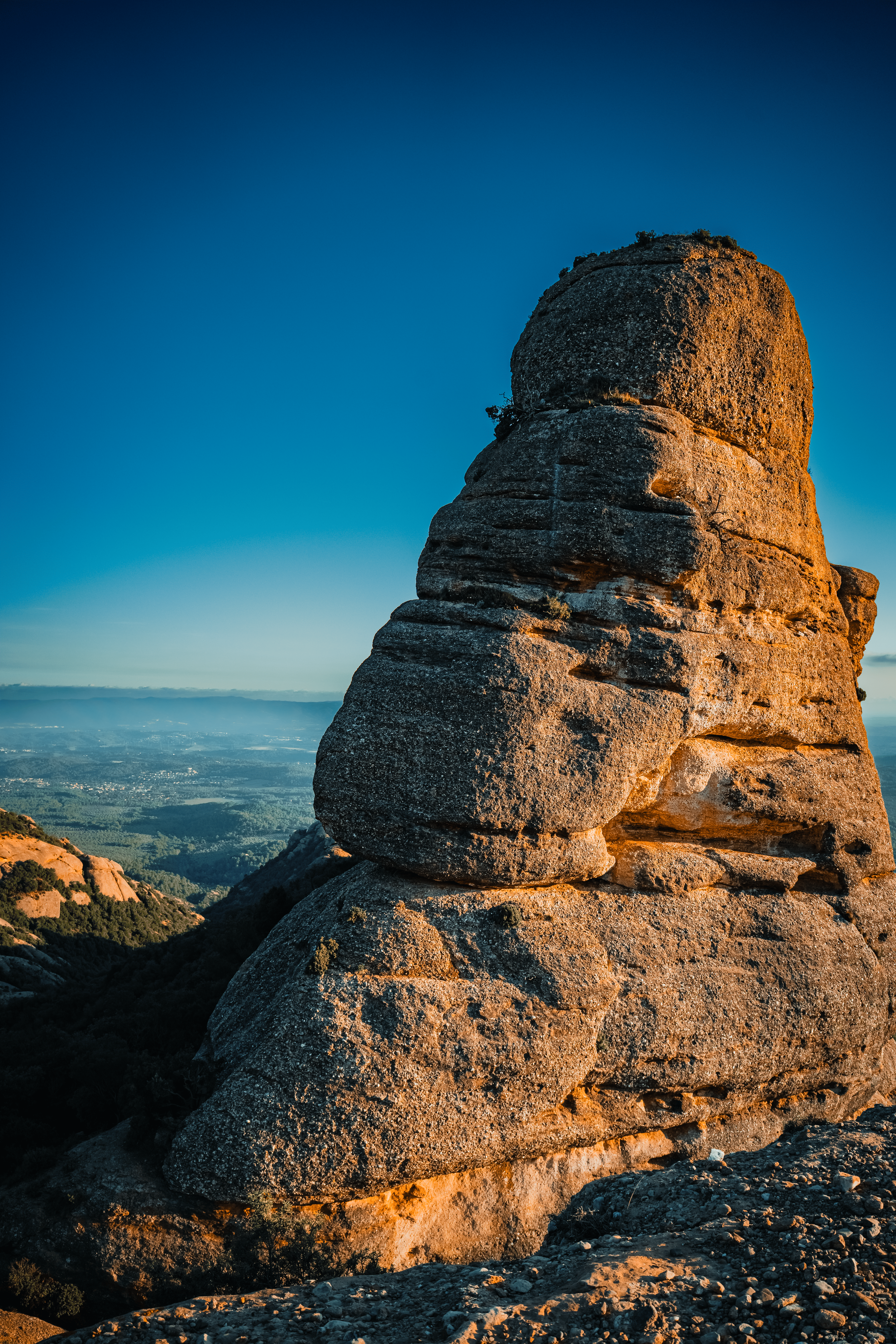Formaciones rocosas en la cima de una montaña al atardecer, con un cielo despejado y un paisaje de valle en el fondo.