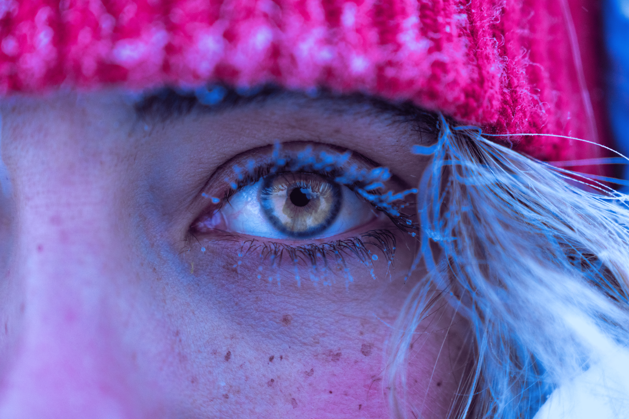 Primer plano del ojo de una persona con maquillaje y un pendiente grande de plumas blancas.