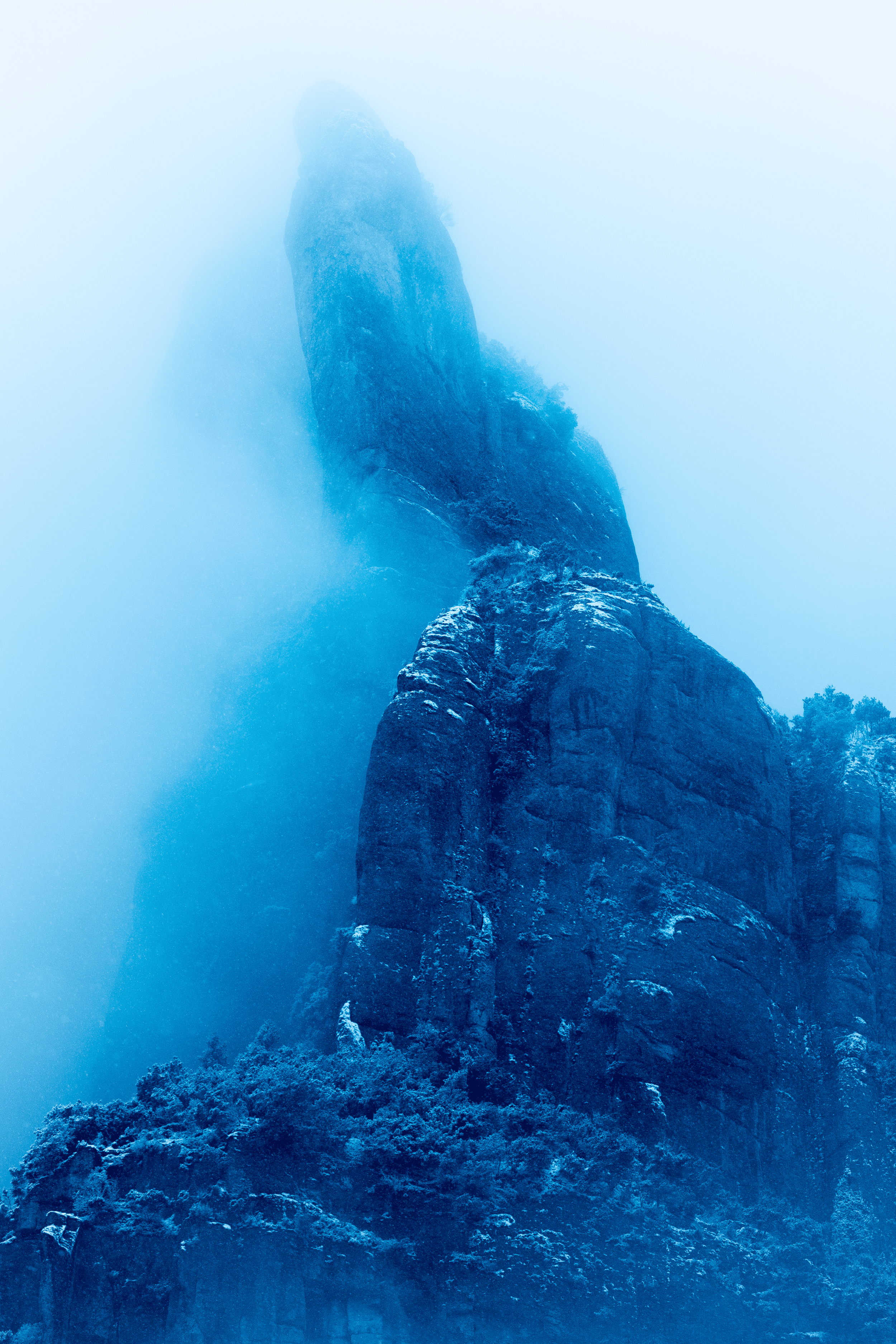 Roca grande y escarpada cubierta de nieve en un entorno de neblina, en un paisaje montañoso.