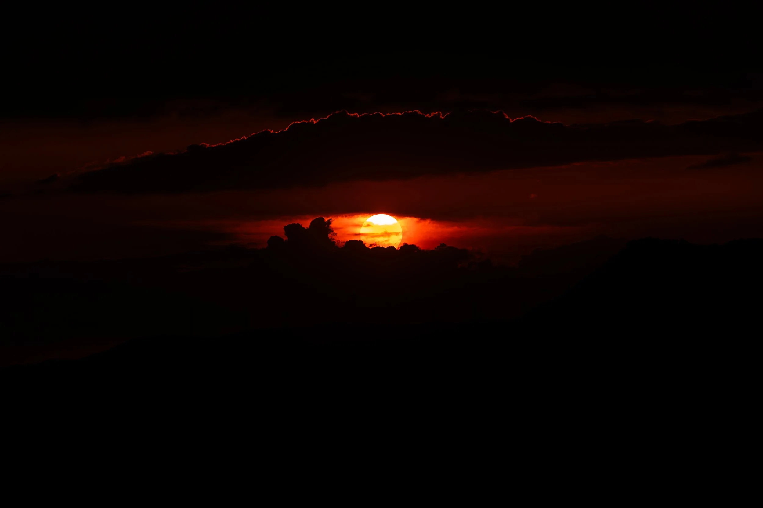 Atardecer con el sol ocultándose detrás de nubes oscuras en el horizonte.