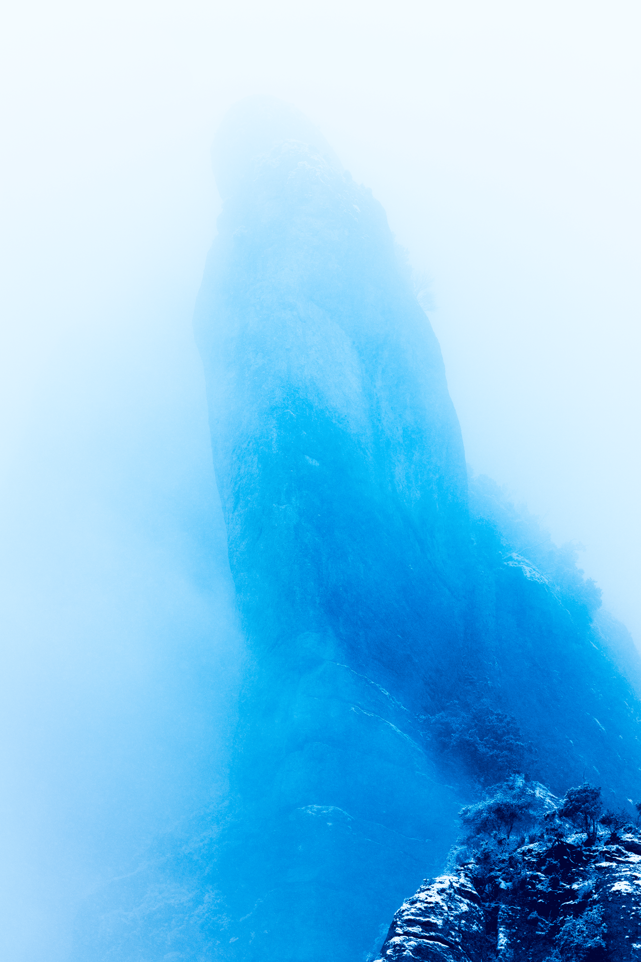 Una montaña rocosa cubierta de nieve y rodeada de niebla.