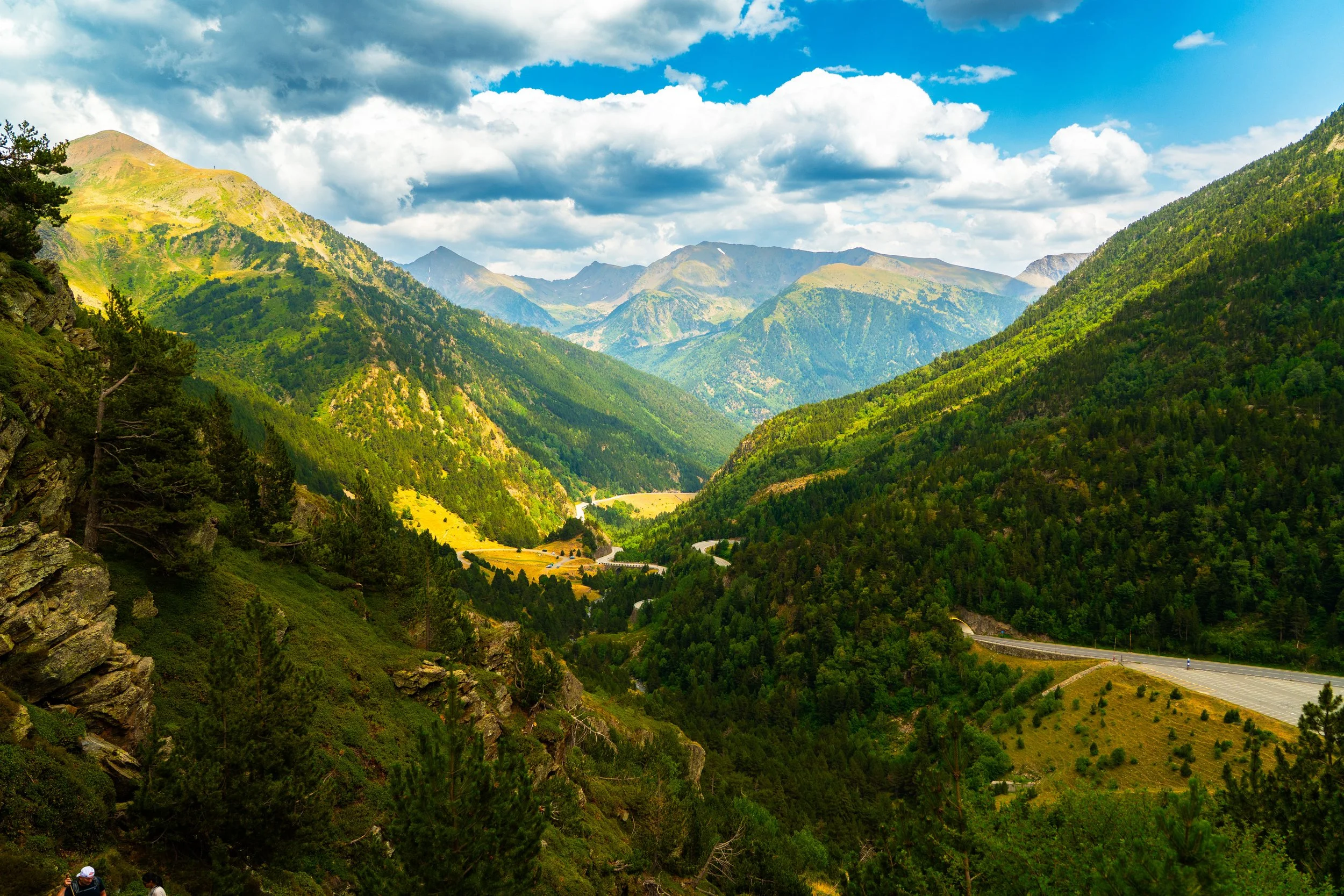 Vista panorámica de montañas verdes con camino serpenteante y cielo con nubes.