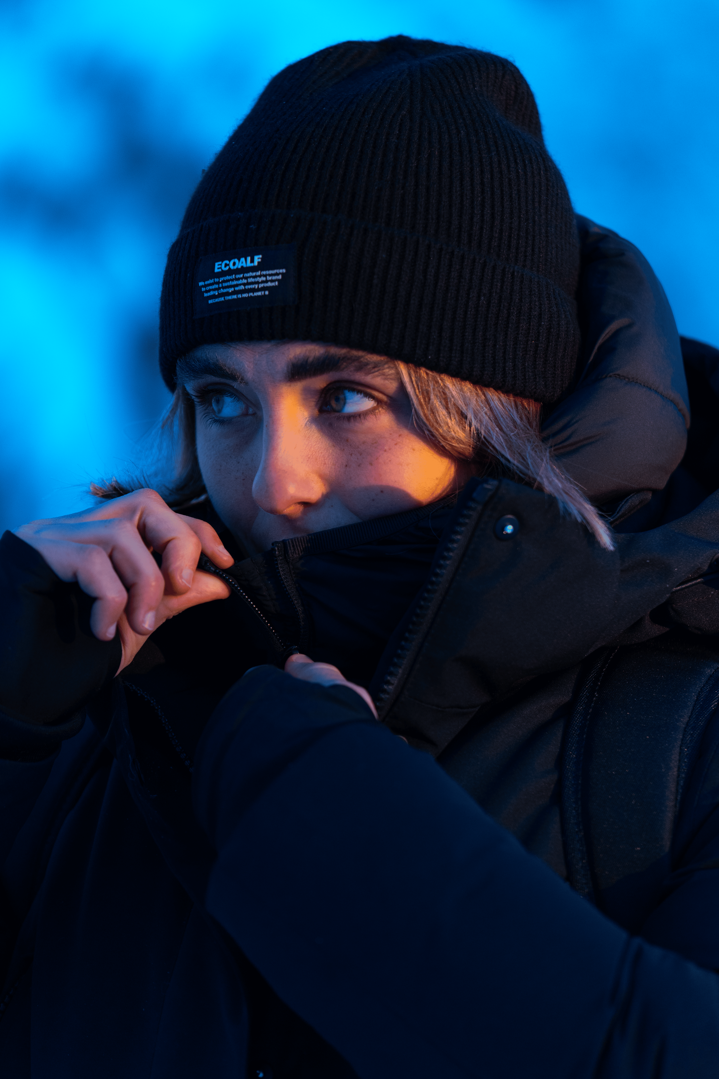 Joven con gorro y abrigo preparado para clima frío ajustando el collar de su chaqueta.