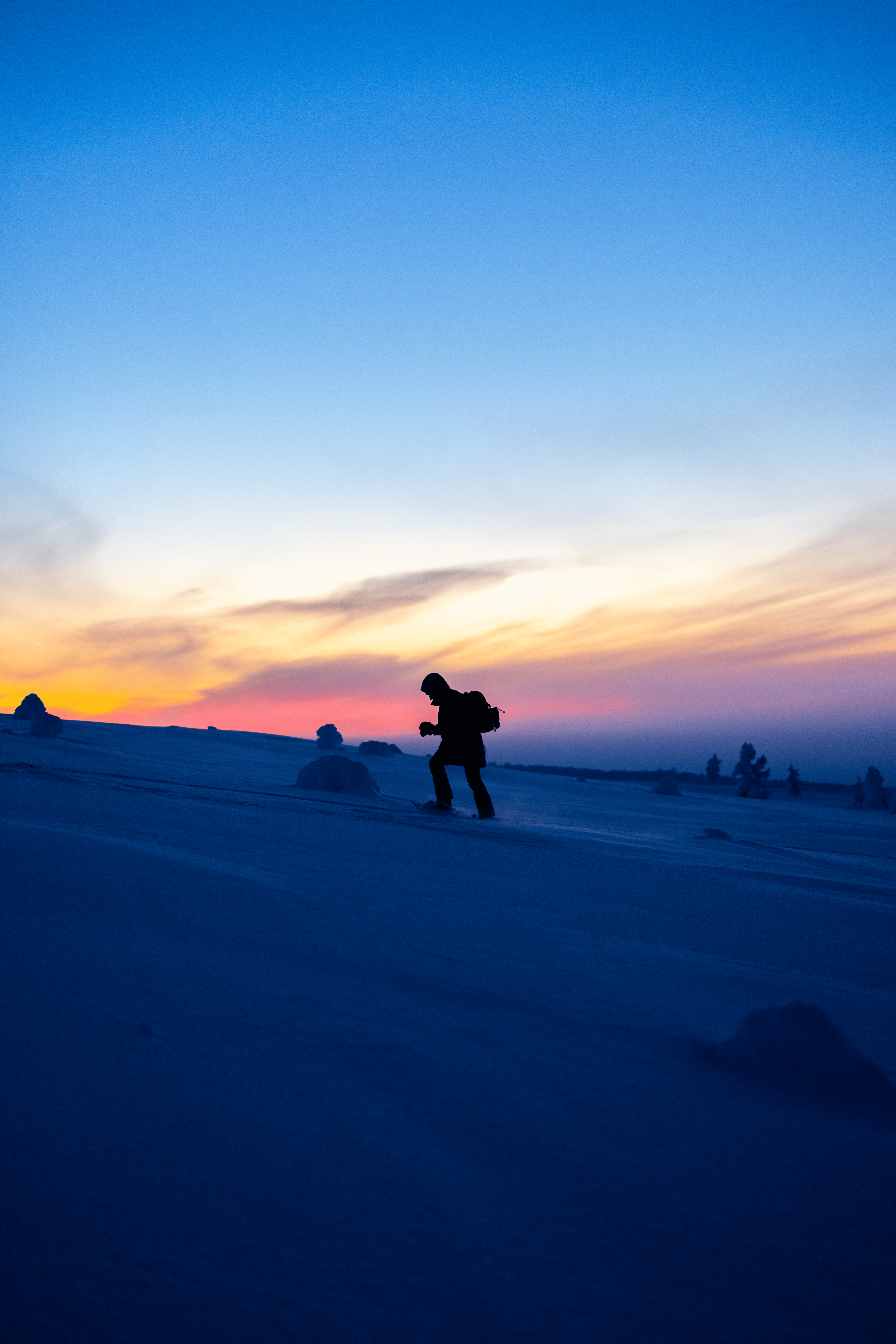 Persona esquiando en la nieve durante el atardecer, con un cielo colorido de tonos naranjas, rosados y azules claros.