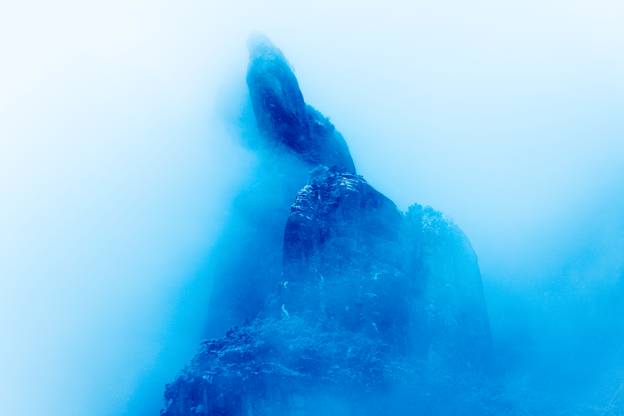 Una montaña rocosa envuelta en niebla o nubes, con vegetación en la base.