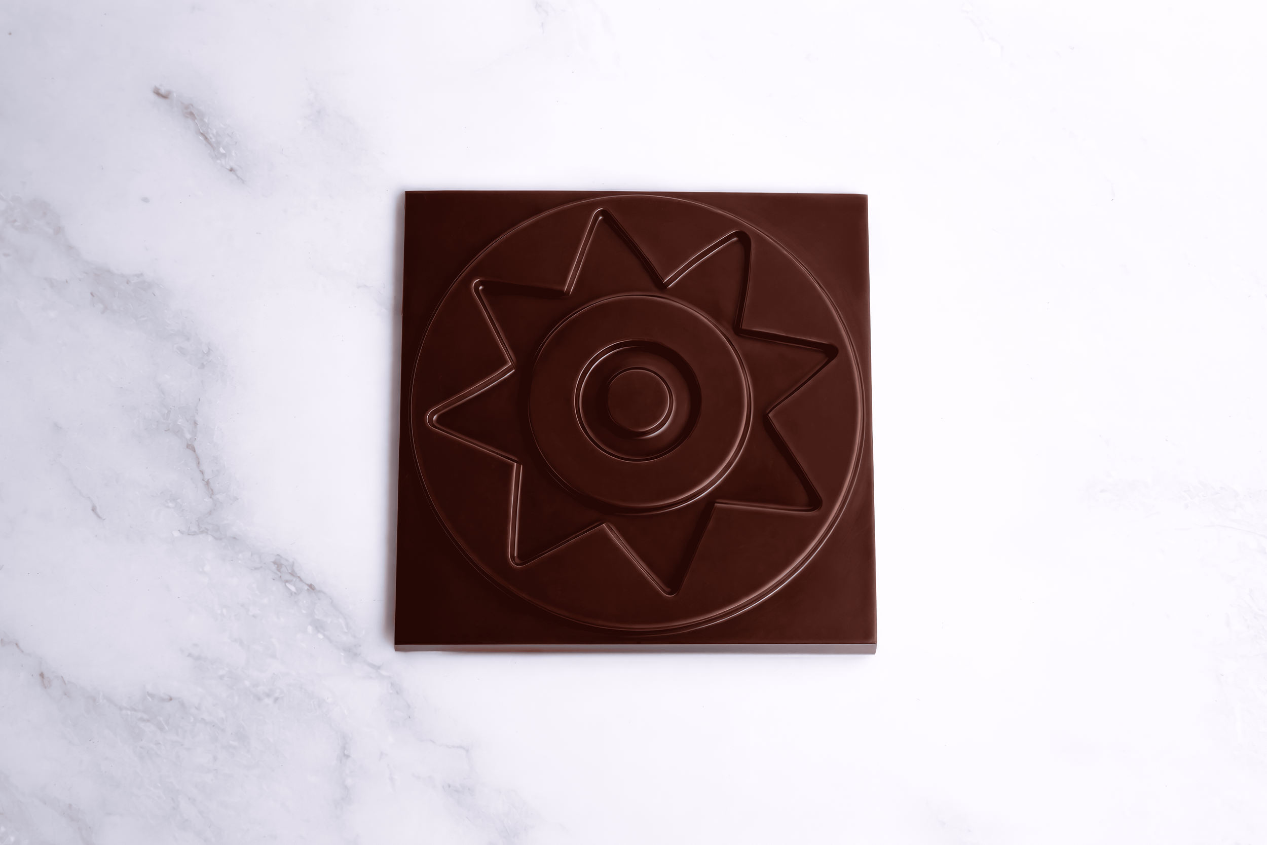 Tableta de chocolate con forma de sol en una superficie de mármol blanco