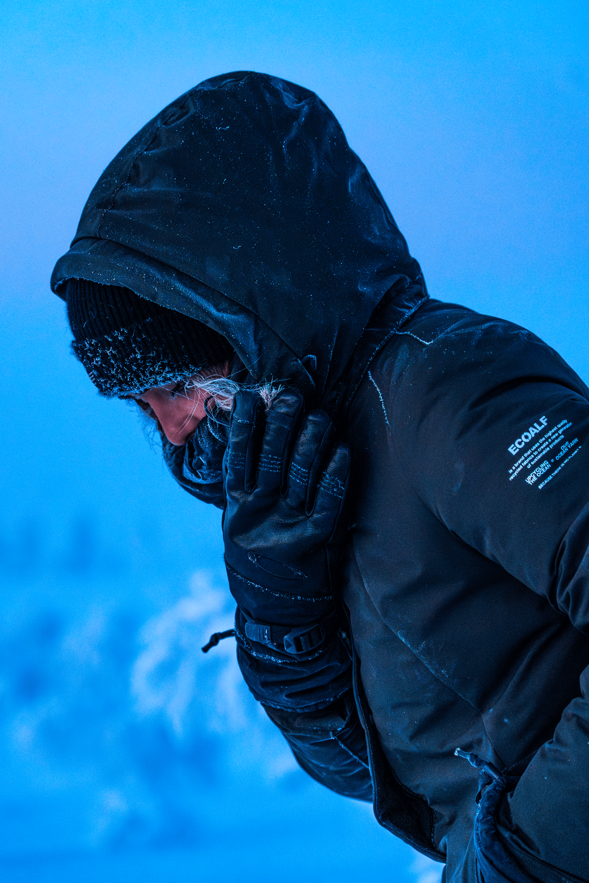 Persona con ropa de abrigo y guantes, con la cabeza agachada, en un entorno frío o nevado.