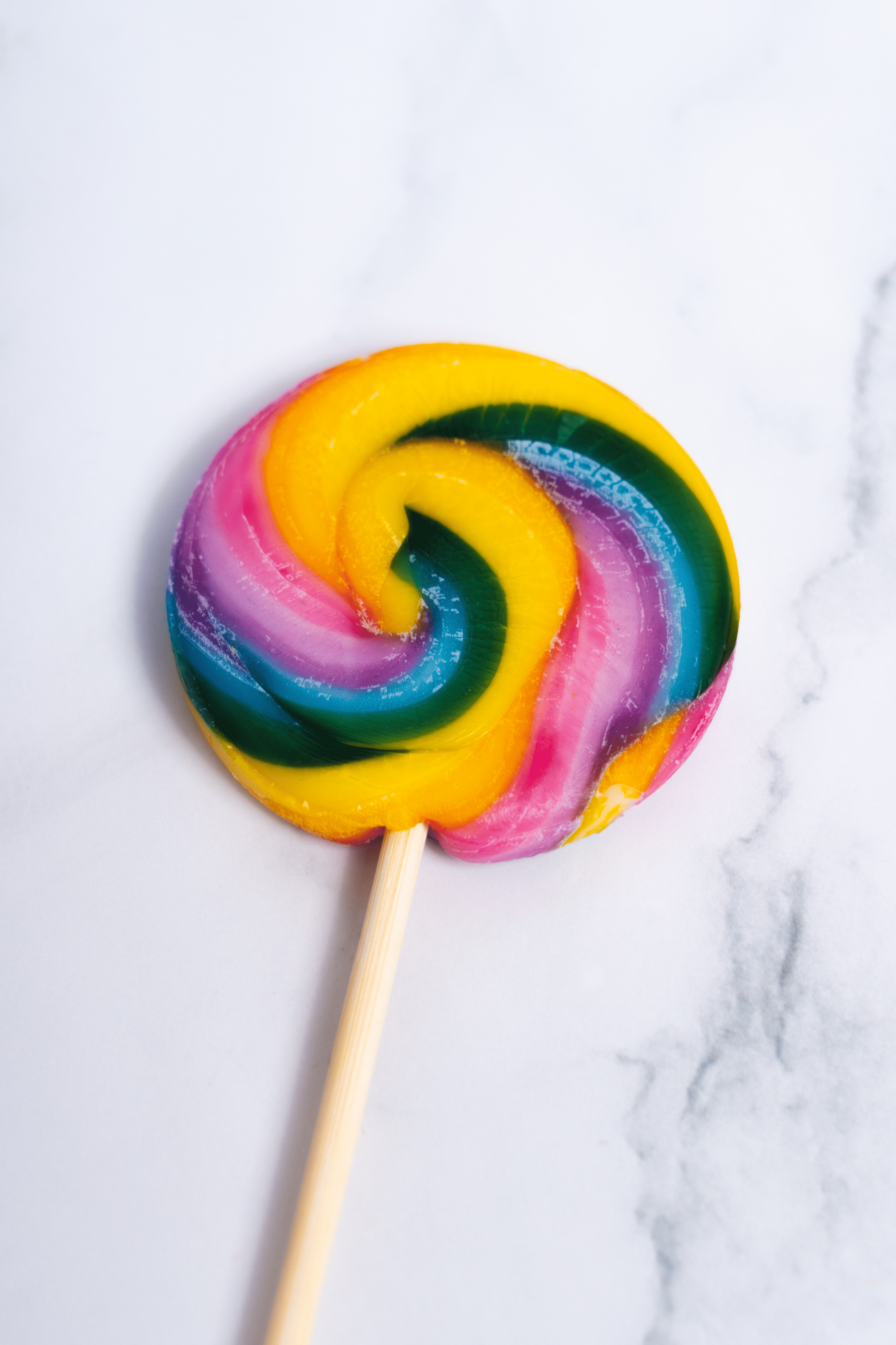 Dulce de azúcar en forma de espiral con colores vibrantes y palo de madera, sobre superficie de mármol