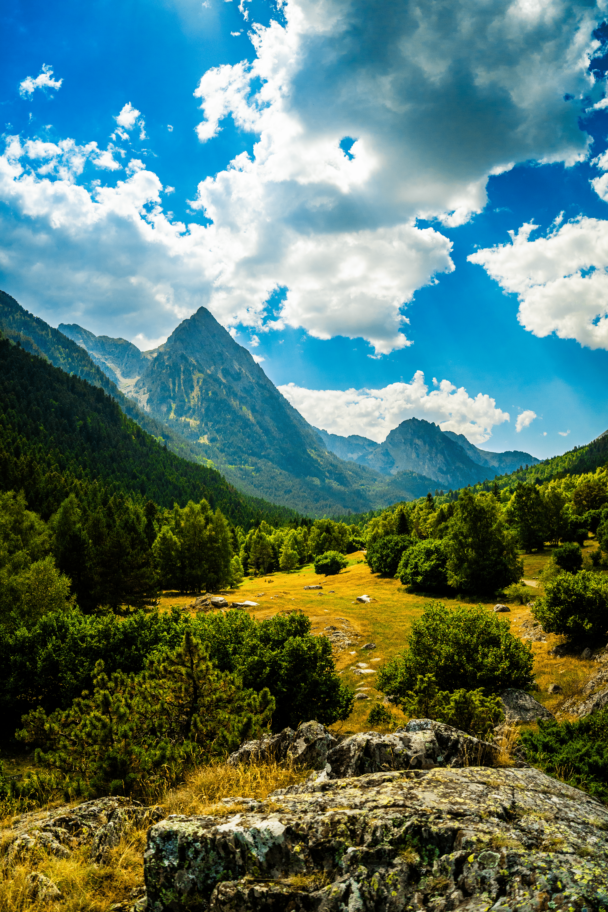 Paisaje montañoso con picos rocosos y vegetación verde, bajo un cielo azul con nubes.