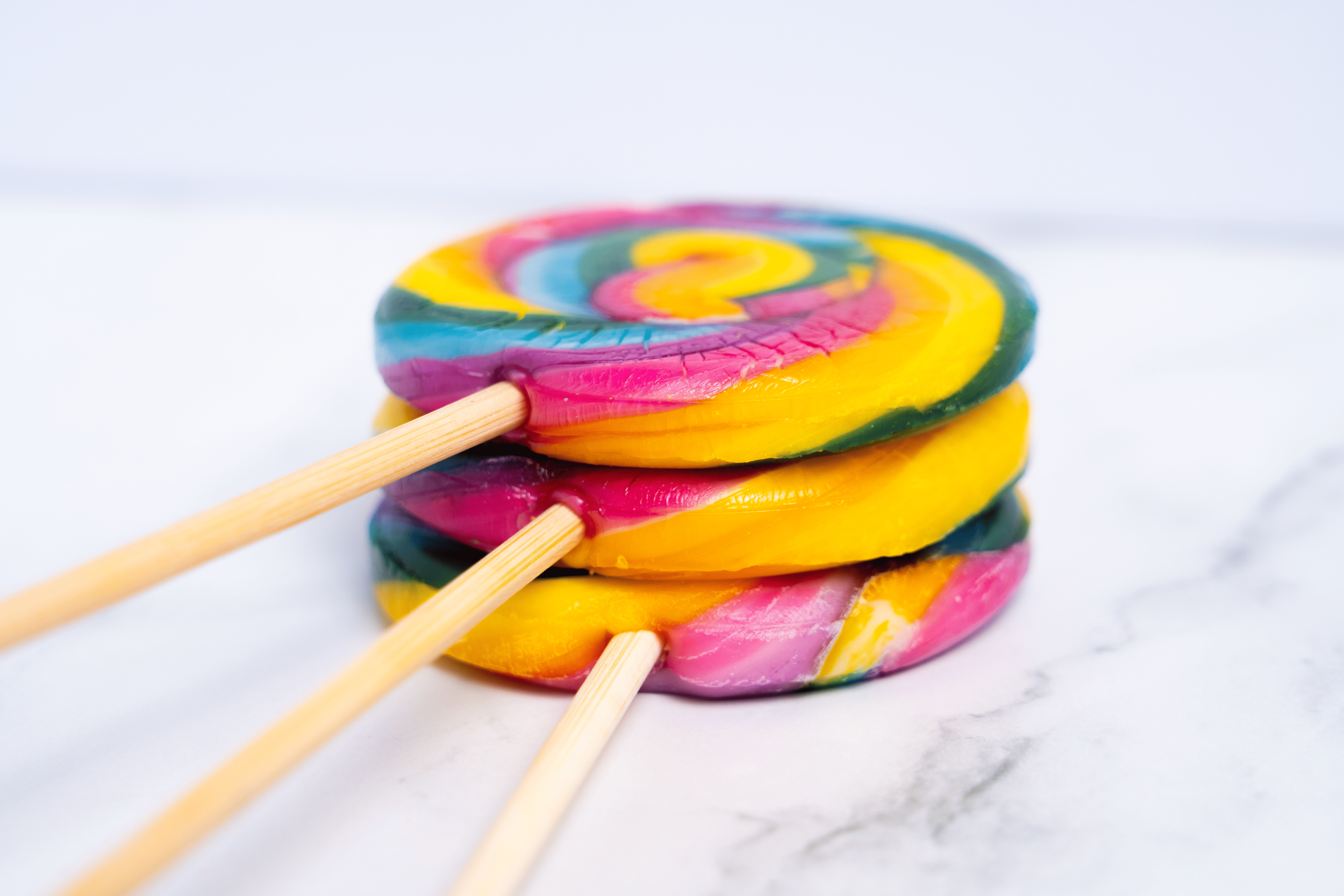 Caramelos de colores en forma de espiral apilados con palitos de madera sobre una superficie blanca.