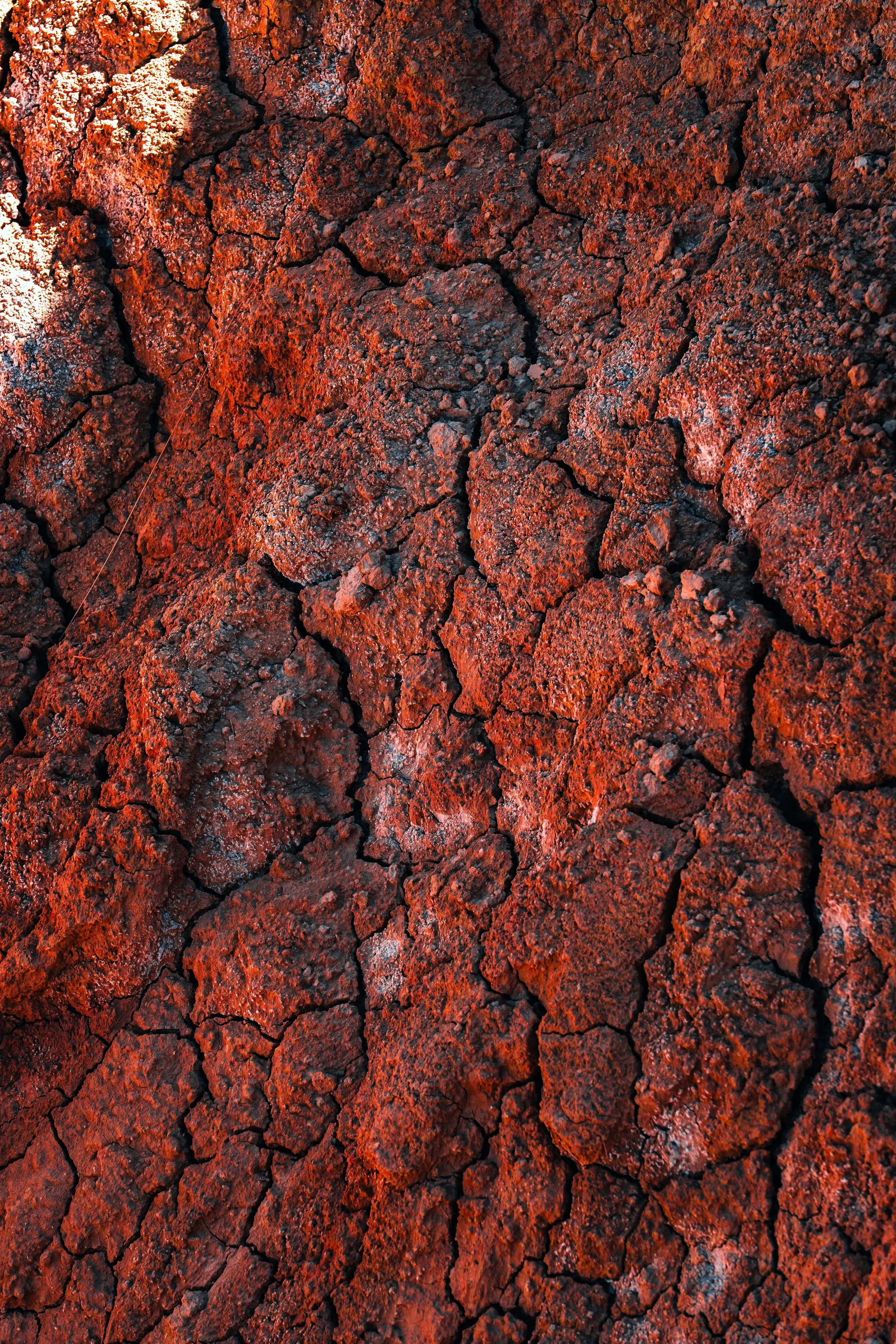 Vista cercana de lava solidificada, de color rojo oscuro con grietas y textura áspera.