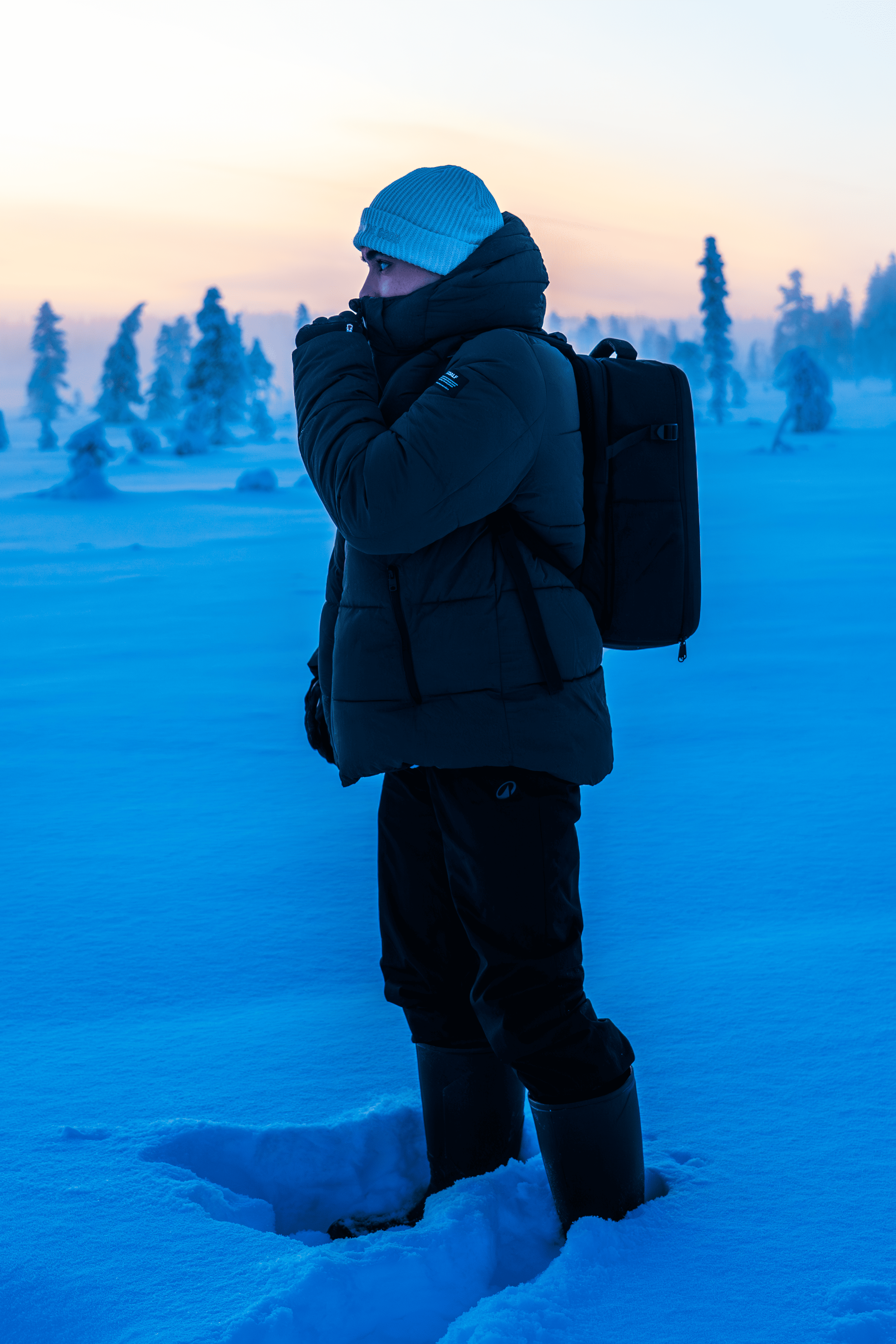 Persona con ropa de invierno, bufanda y mochila en un paisaje nevado, mirando al horizonte en un entorno frío y desolado.