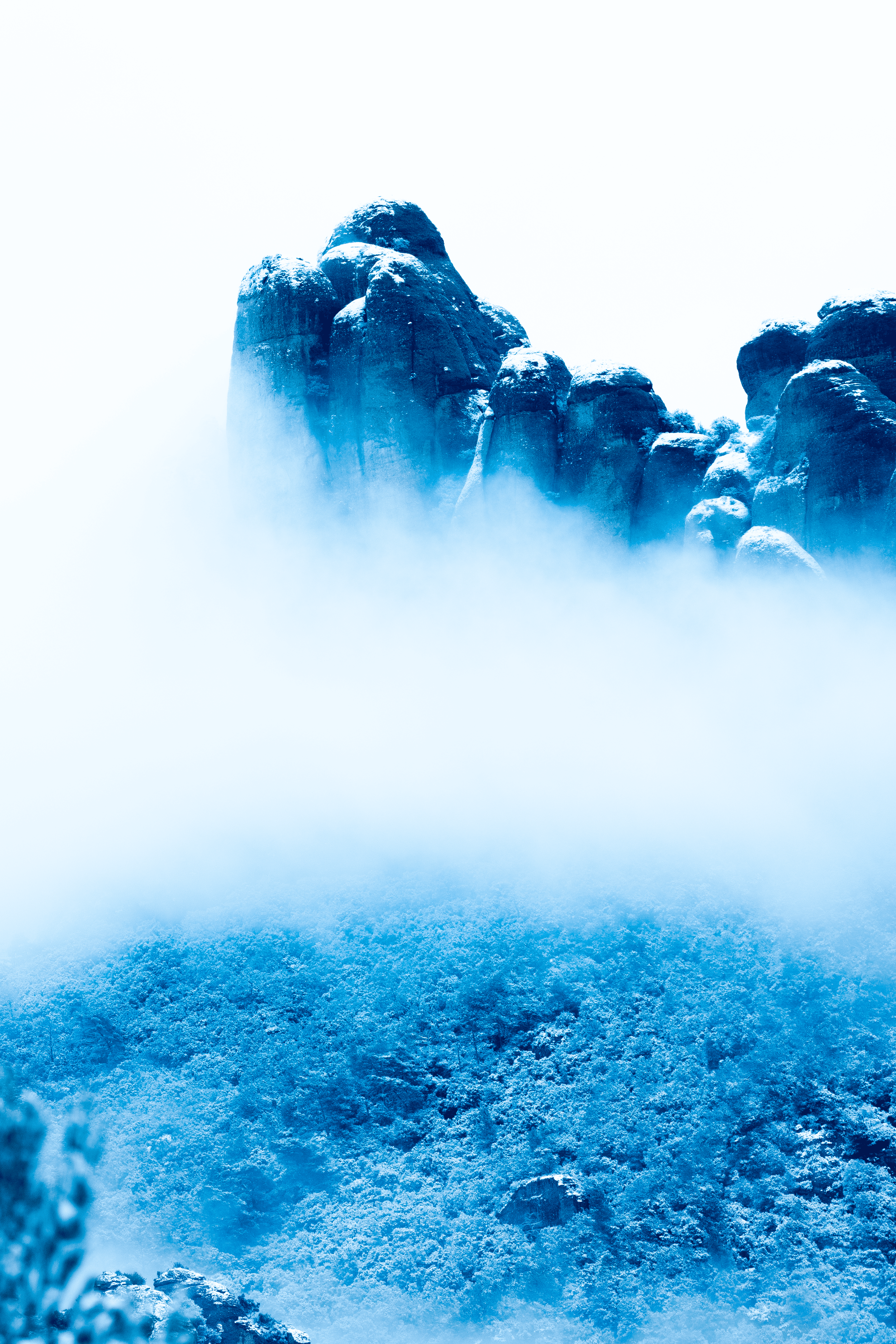 Montaña rocosa cubierta de nieve, rodeada de nubes y niebla, en tonos azules y blancos.