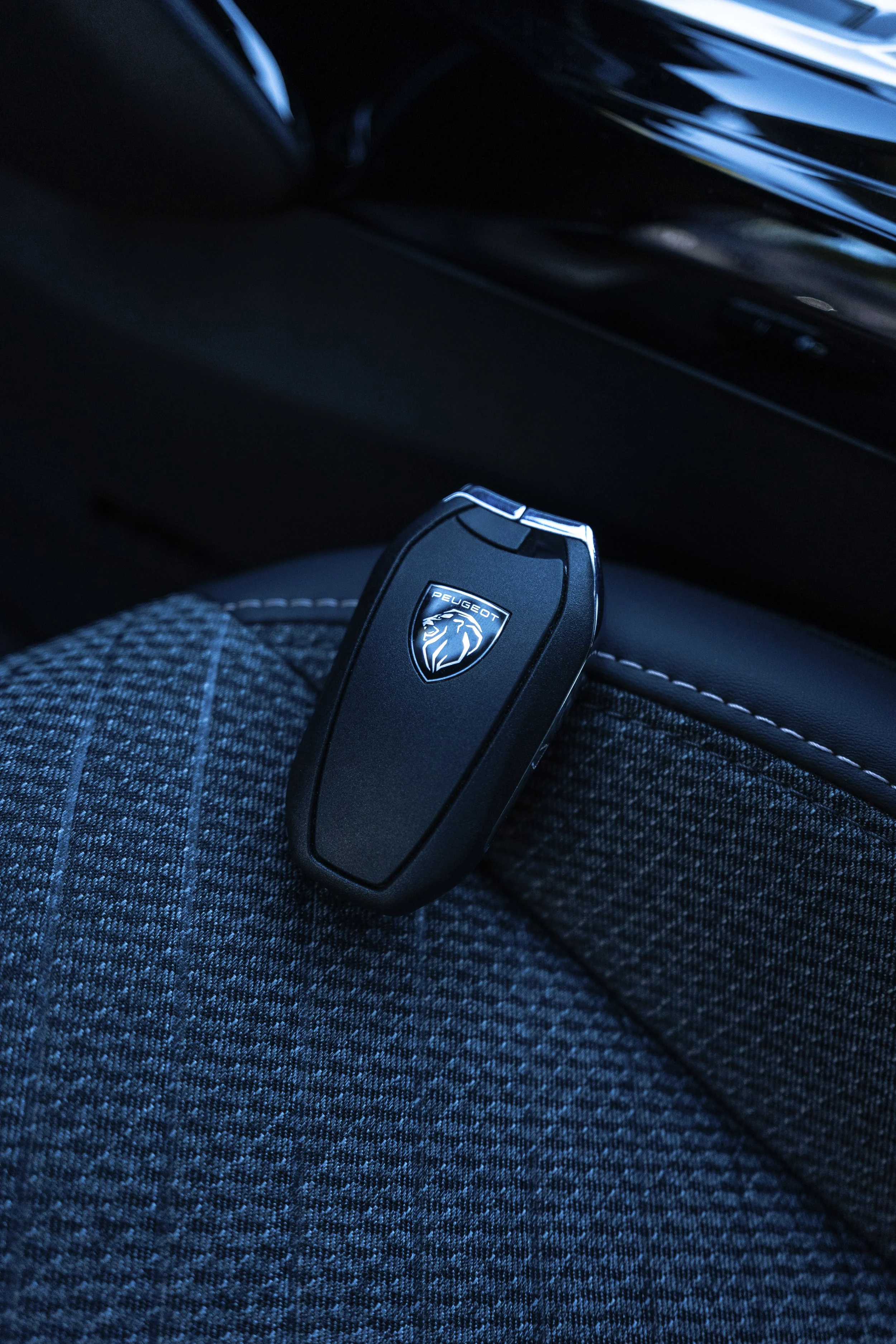 Llave de coche Peugeot sostenida en la pierna de una persona que lleva pantalones de mezclilla oscuros con líneas blancas.