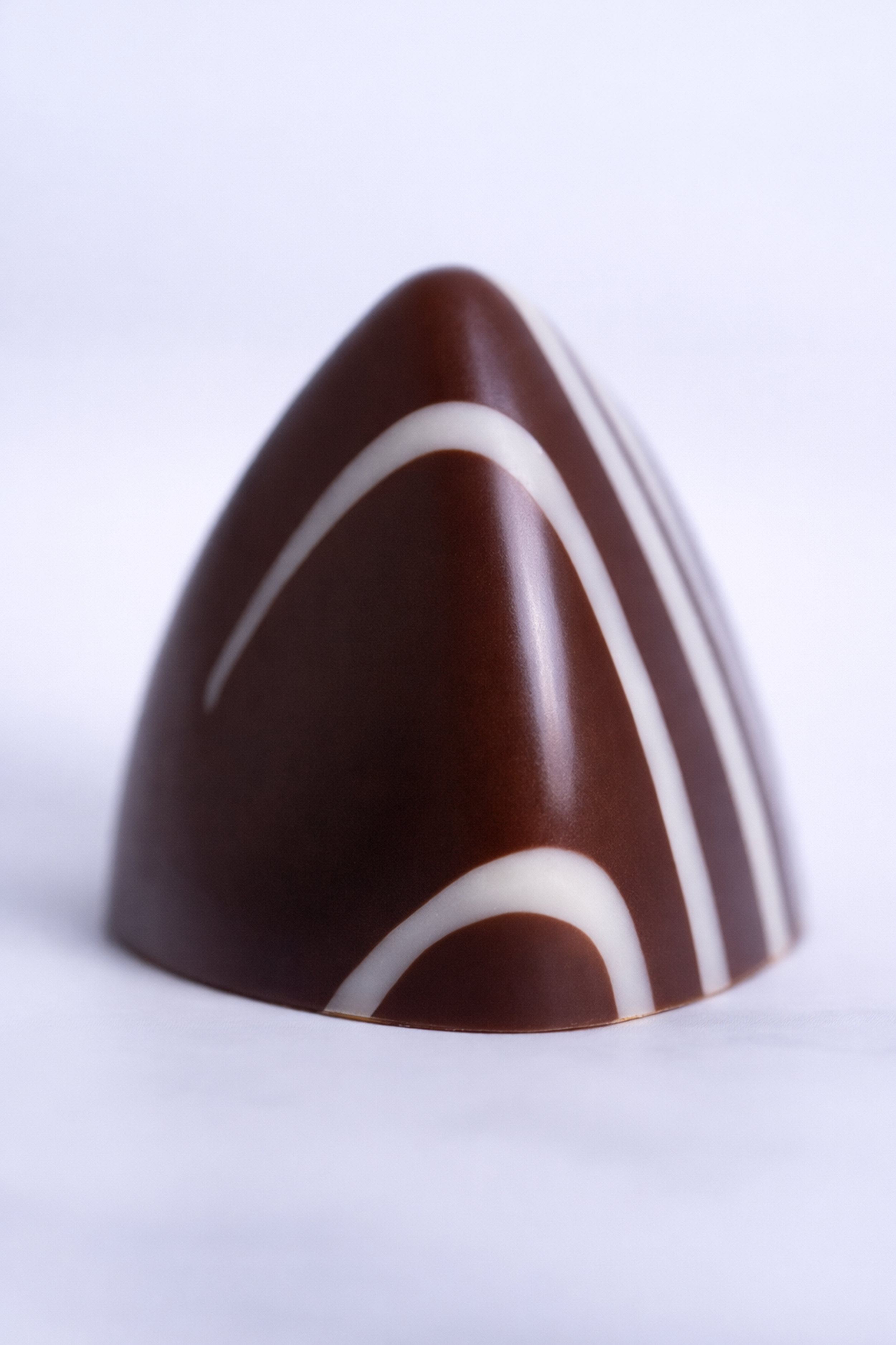 Chocolate con forma de pirámide decorada con líneas blancas.