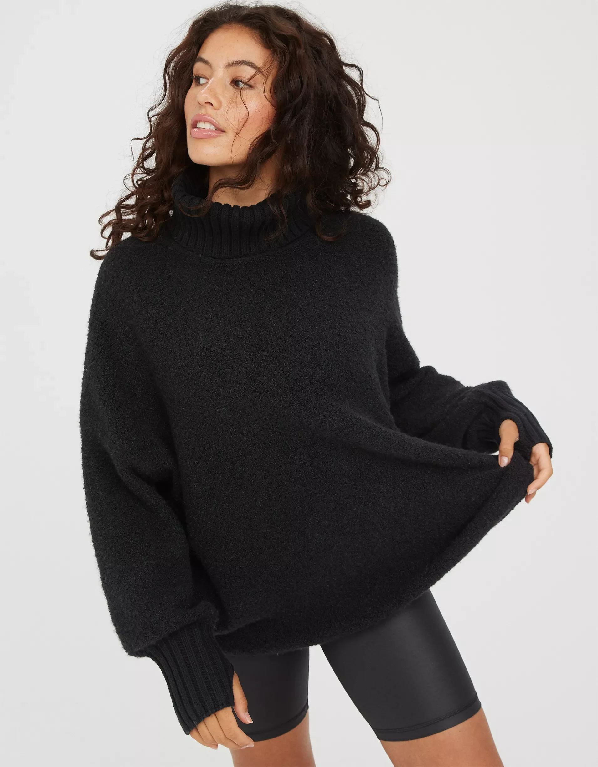 Woman in black turtleneck sweater and black shorts posing on white background