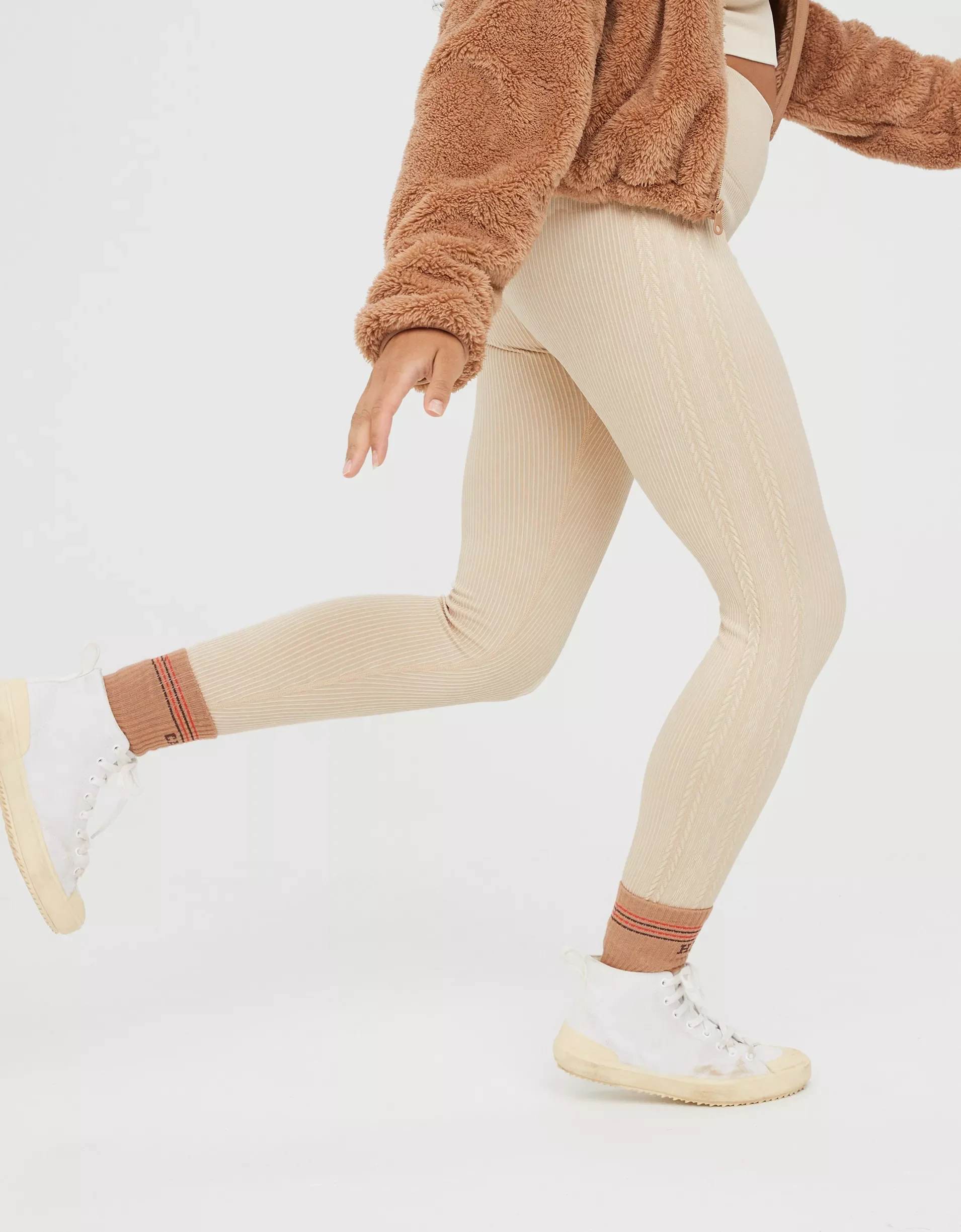 A person wearing beige ribbed leggings, white sneakers, and brown socks, with a beige and brown fuzzy jacket.