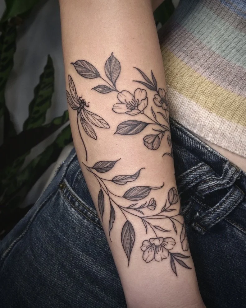 Line drawing of a floral tattoo with flowers, leaves, and a butterfly on a person's forearm.