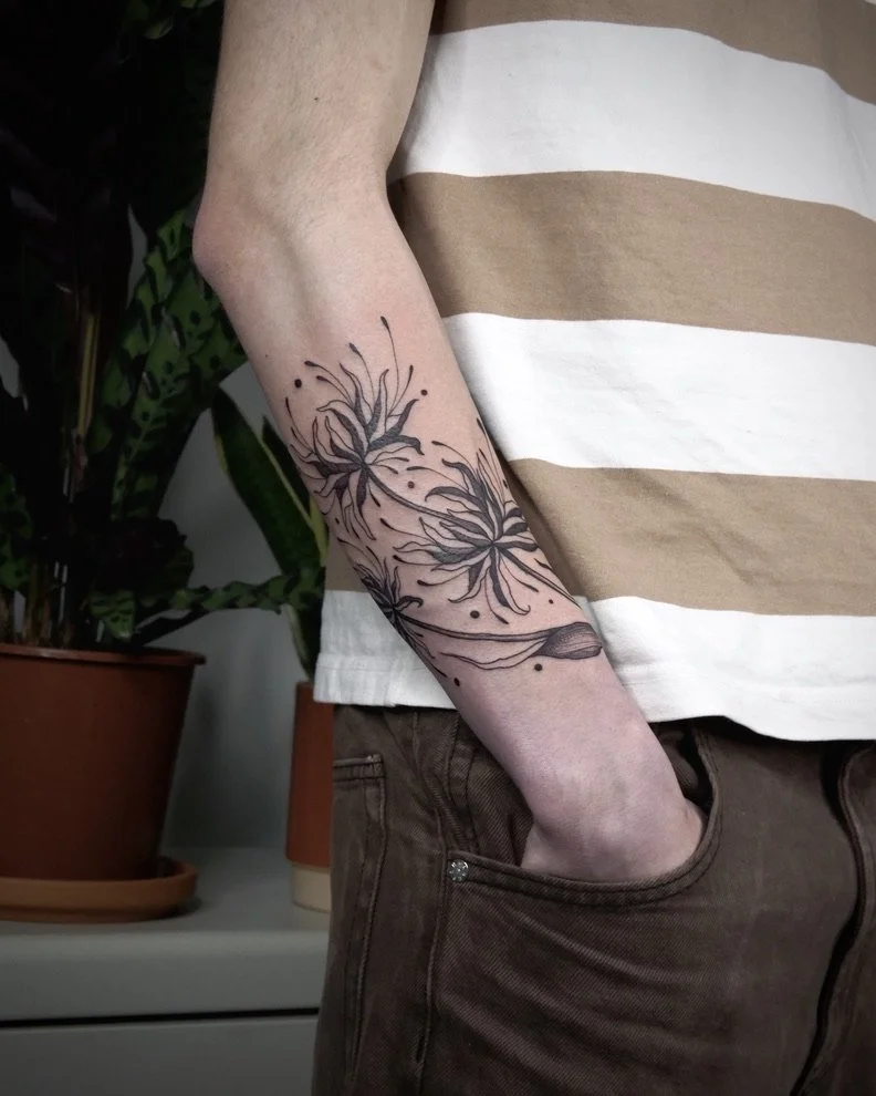 A person's arm with a black floral tattoo, wearing a beige and white striped shirt, and their hand resting in the pocket of brown pants.