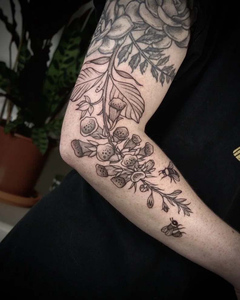 Black ink outline tattoo of berries, leaves, and a bee on a person's arm.