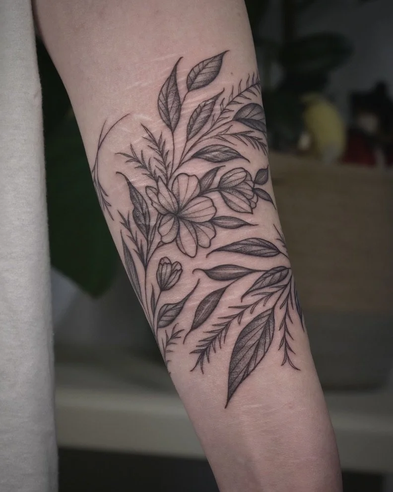 Black ink floral tattoo on a person's forearm featuring various detailed leaves and flowers.